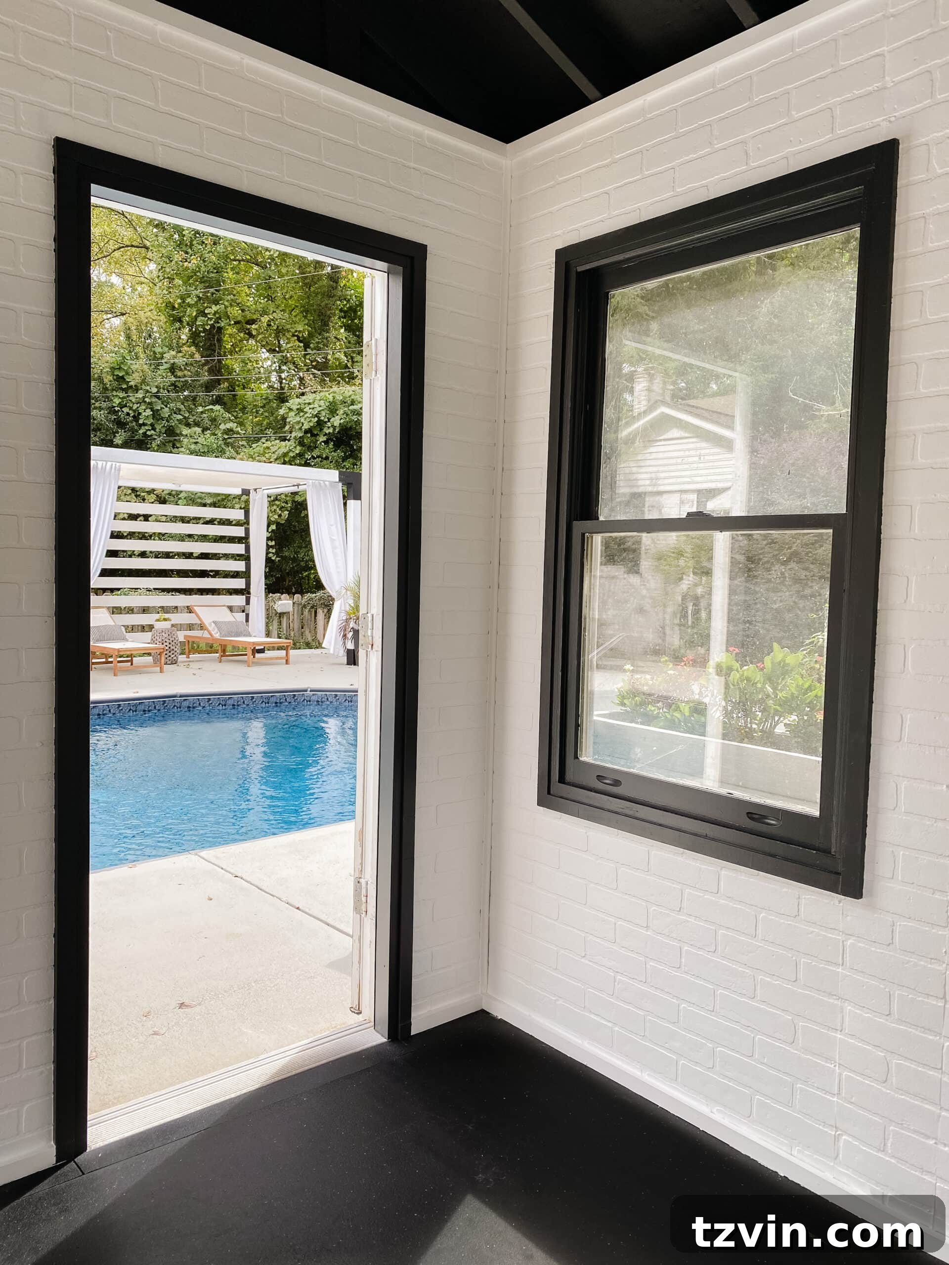 Faux Brick Gym Shed Upgrade 19 View from inside the home gym, showing white brick walls and black trim, with a glimpse of the poolside area outside.