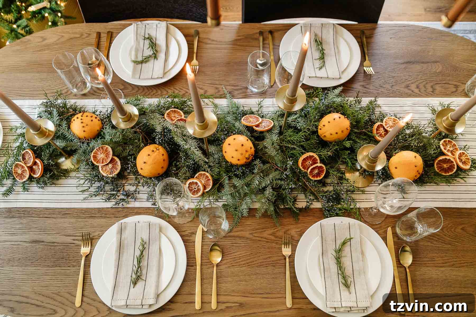 simple Christmas table centerpiece idea using fresh cut evergreen, juniper berries, dried orange slices, orange pomanders, and gold candle holders