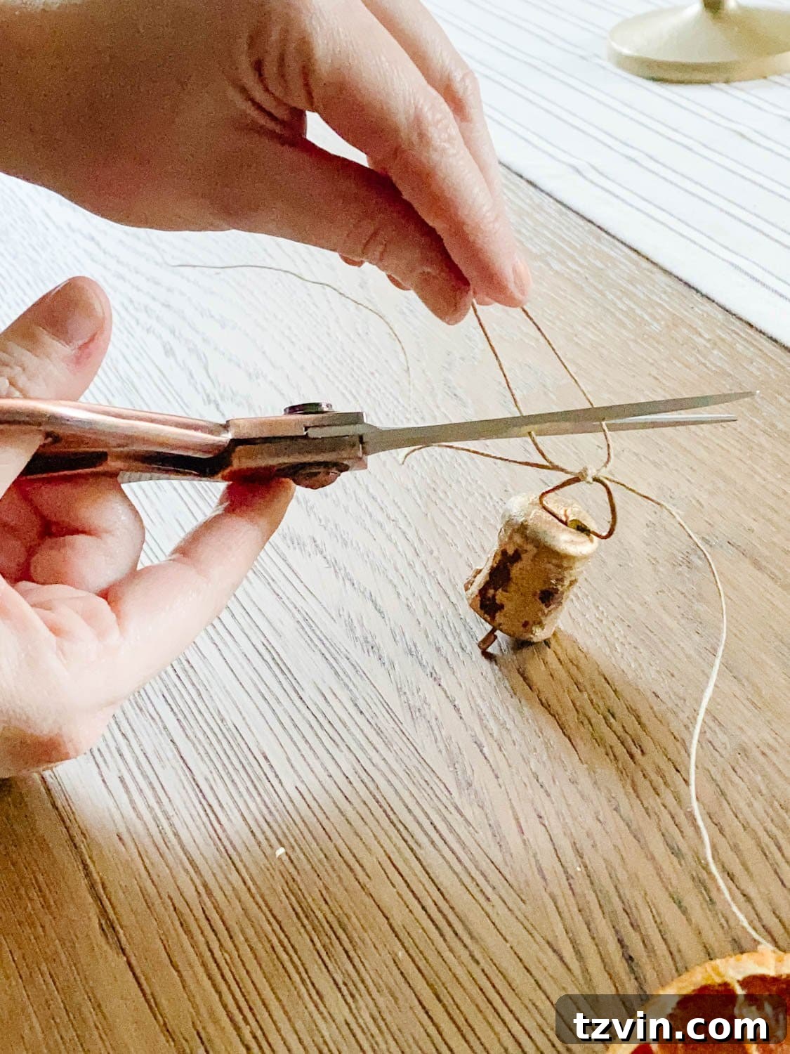 Craft Your Own Beautiful Dried Orange Garland 11 A hand using scissors to trim the excess twine from a tied mini brass bell on the garland for a clean look.