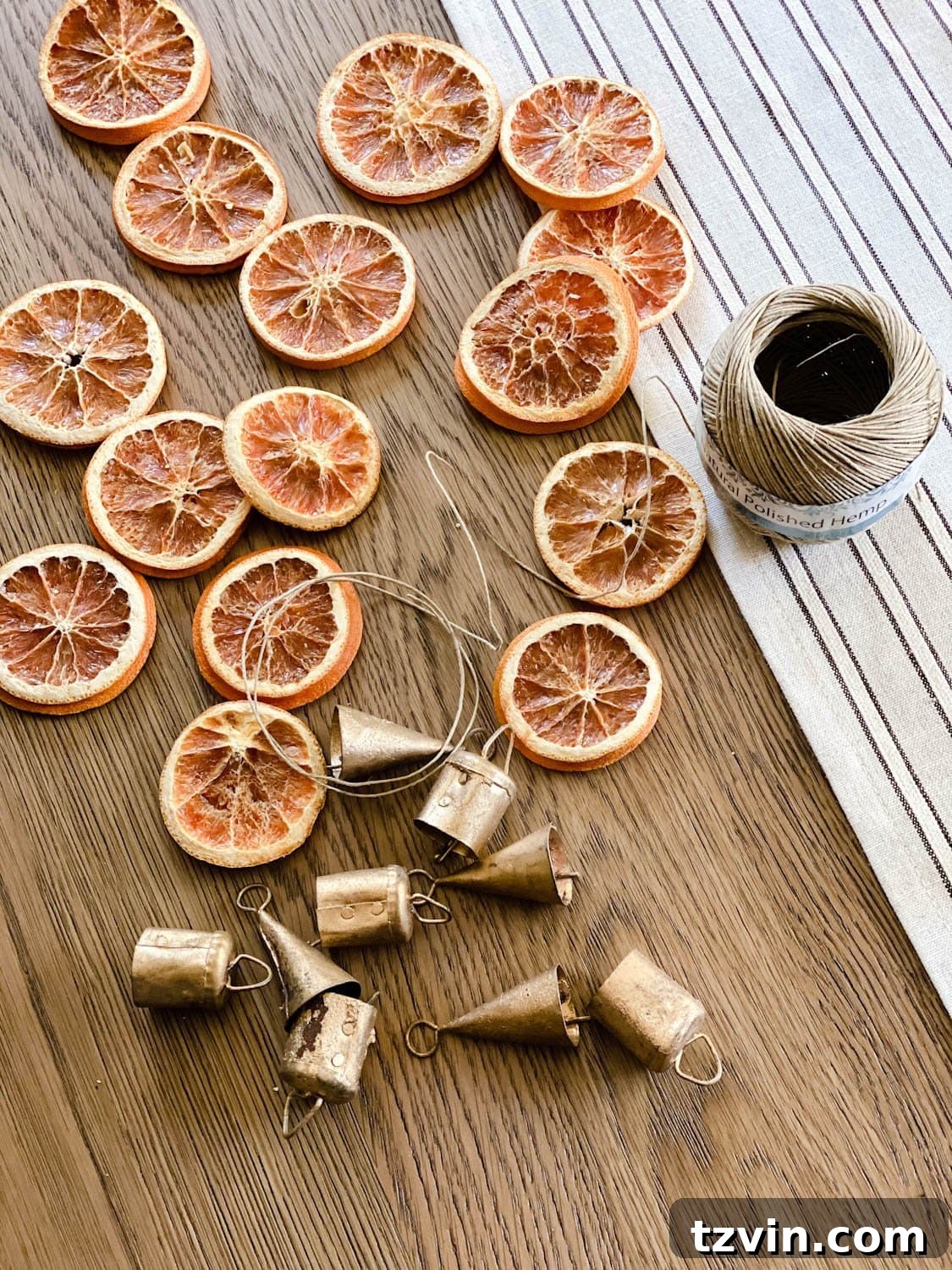 Craft Your Own Beautiful Dried Orange Garland 4 A flat lay showing various supplies needed for making dried orange garland: dried orange slices, hemp twine, scissors, and mini brass bells.