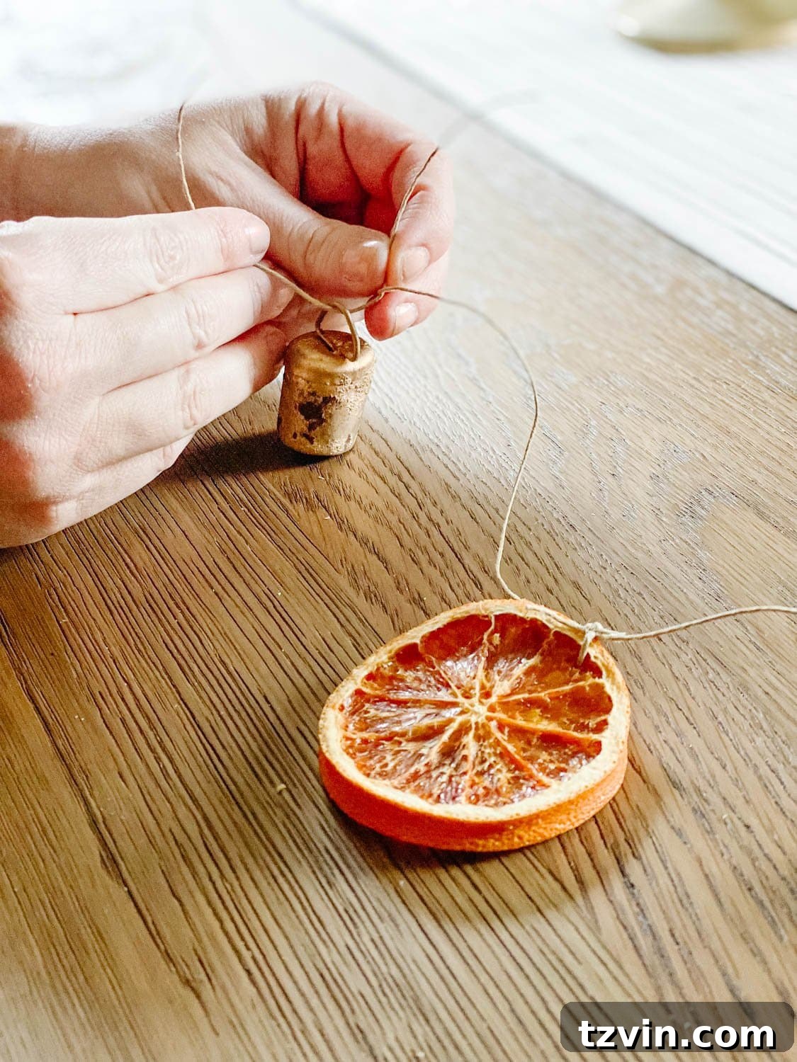 Craft Your Own Beautiful Dried Orange Garland 9 A hand tying a small brass bell onto the dried orange garland, demonstrating the embellishment process.