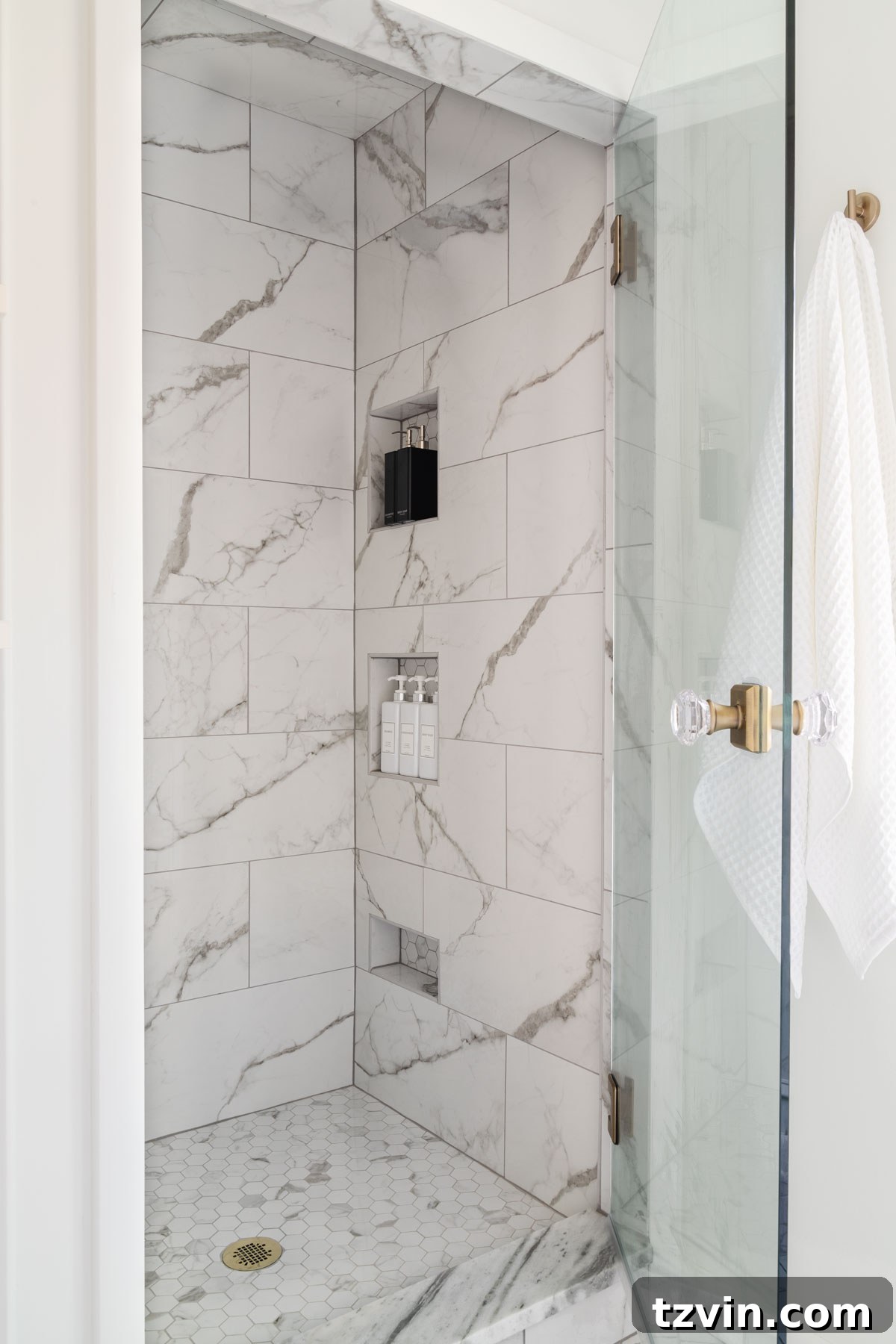 Marble look ceramic tile shower with shower niches and glass shower door