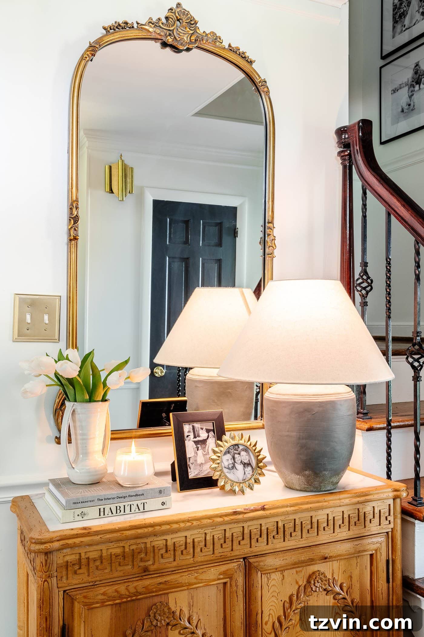 Mastering Your Entry Table Decor A Pros Step-by-Step Guide 3 entry table decor in a foyer with gold mirror, lamp, vase of tulips, candle, and picture frames on a carved wood cabinet