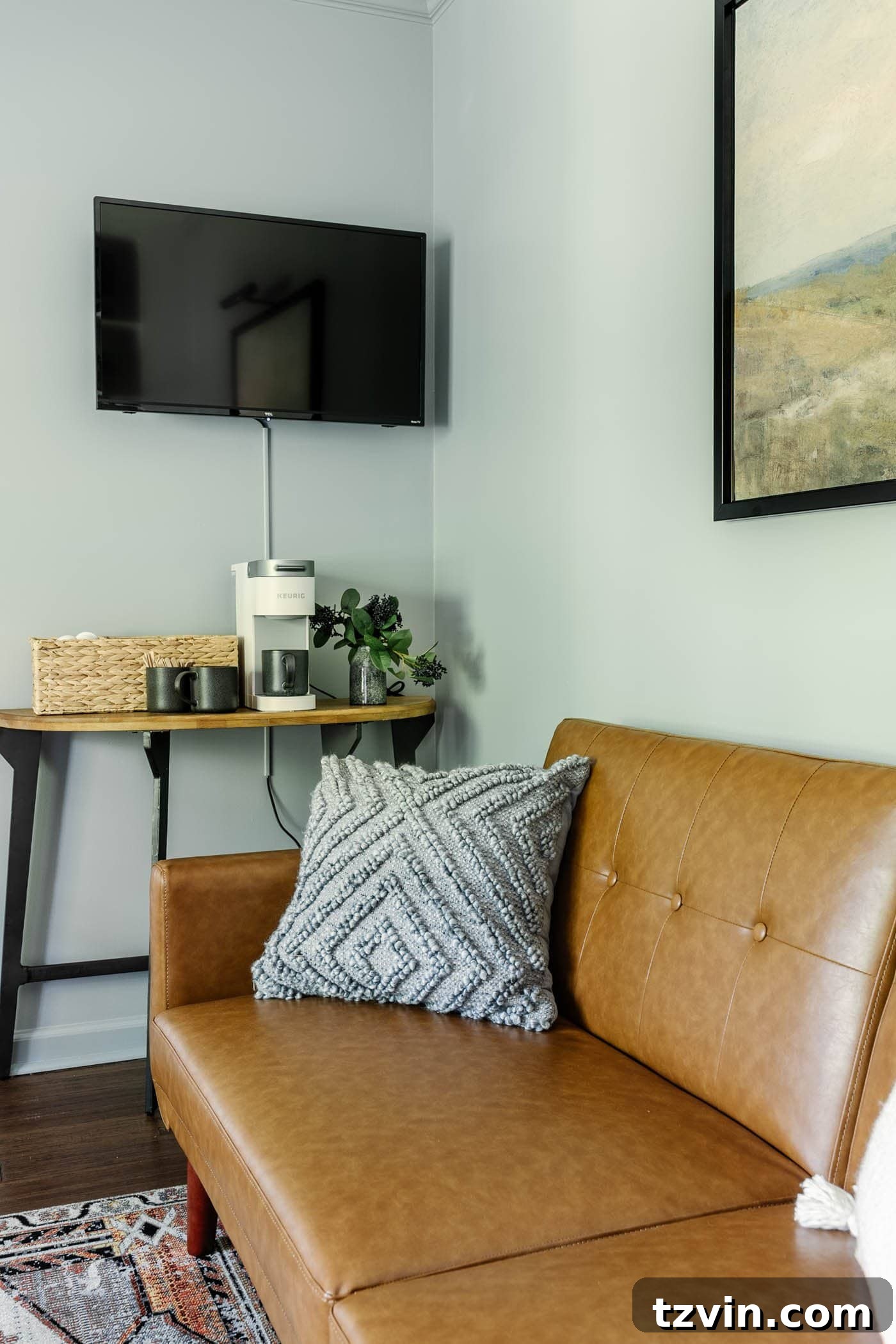 Thoughtfully designed home office featuring a convenient coffee bar table and a wall-mounted TV, providing a welcoming space for guests alongside a comfortable futon.
