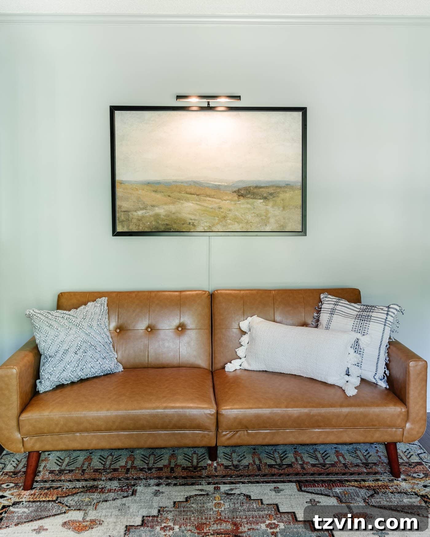 Stylish home office lounge area featuring a comfortable faux leather futon, decorative throw pillows, and a cozy area rug, creating an inviting space for relaxation.