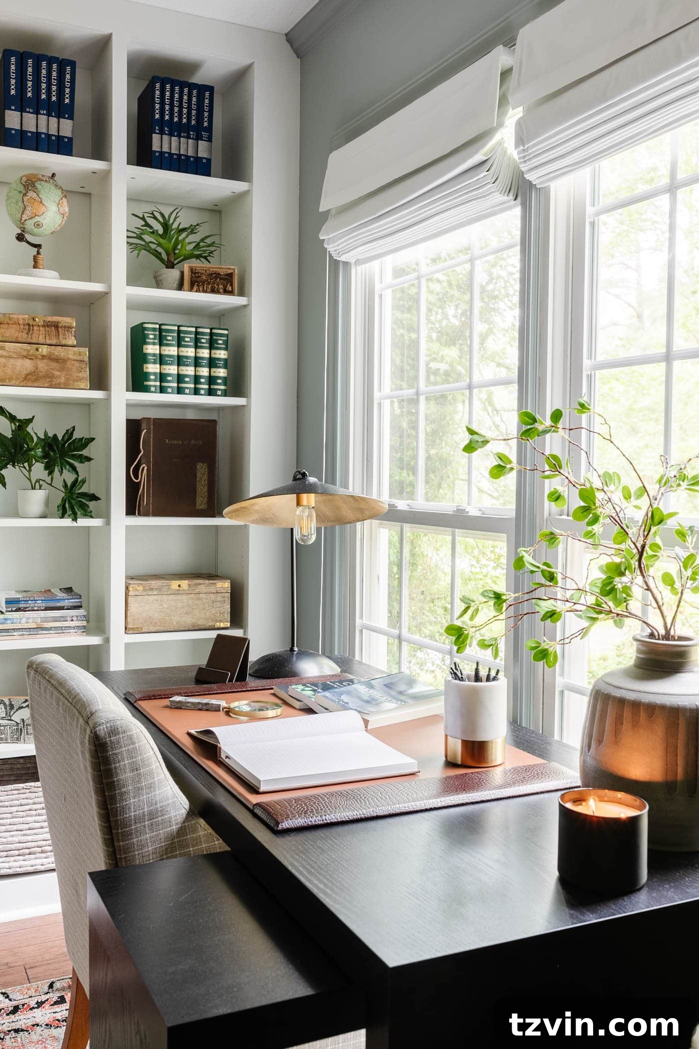Stylish black office desk by a window featuring a leather desk pad, a modern desk lamp, a vase of elegant branches, and integrated shelving for organized storage.