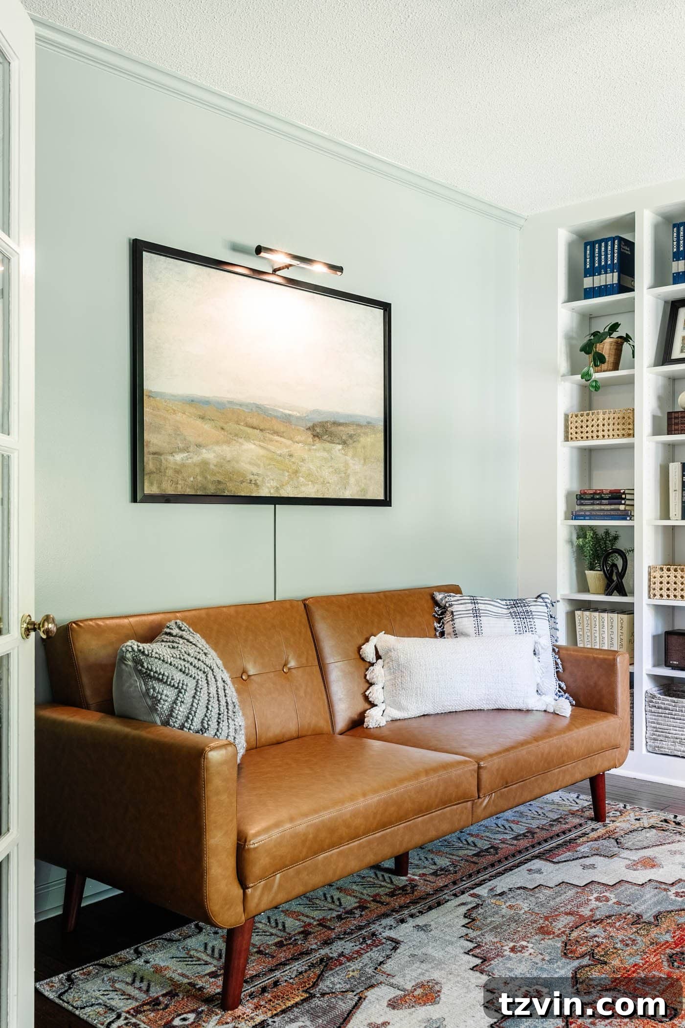 Inviting faux leather futon in a home office lounge area, beautifully complemented by serene landscape art and a subtle picture light, perfect for relaxation or guest accommodation.