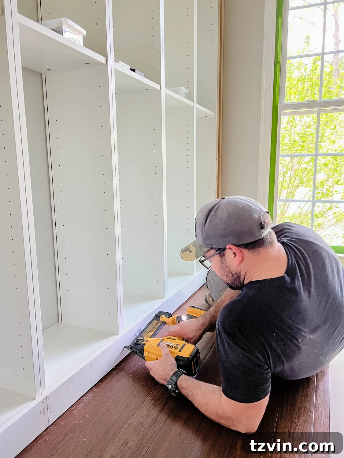 Building Custom Bookshelves with IKEA Billy Bookcase Hacks 18 attaching 1x4 board to the bottom of bookcases using a finish nailer for DIY built in bookshelves