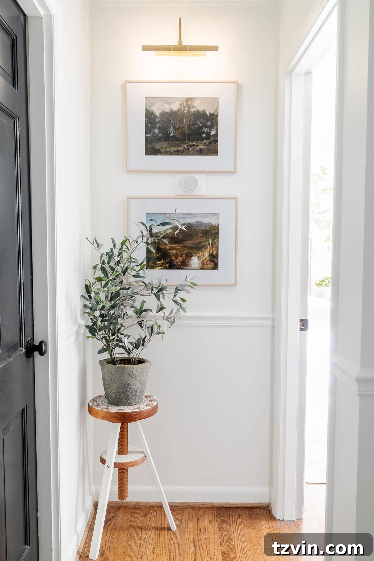 Gold wireless picture light above framed art prints in a hallway, demonstrating cordless convenience