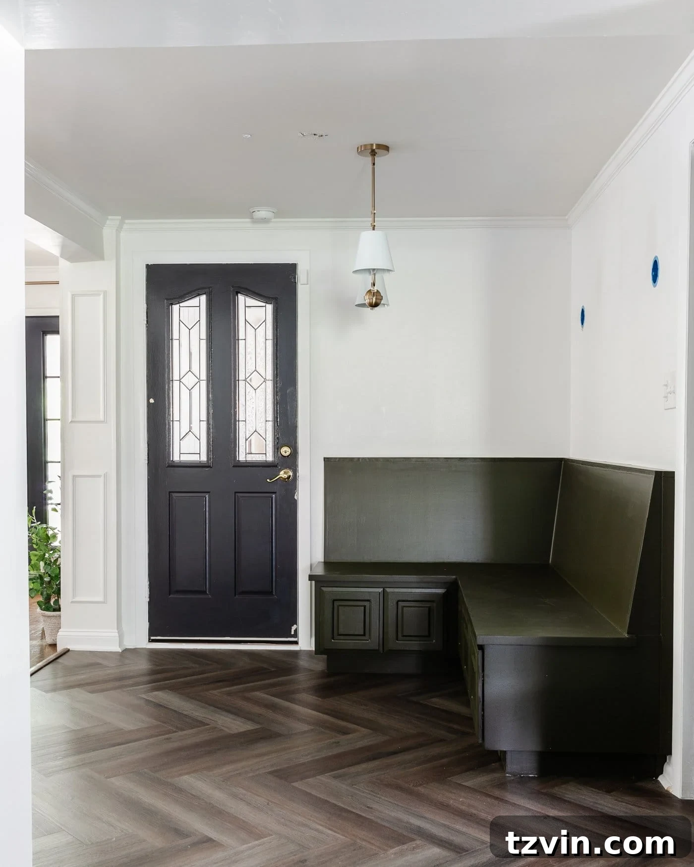 breakfast nook room with olive green corner banquette, black door, white walls, and herringbone LVP floors