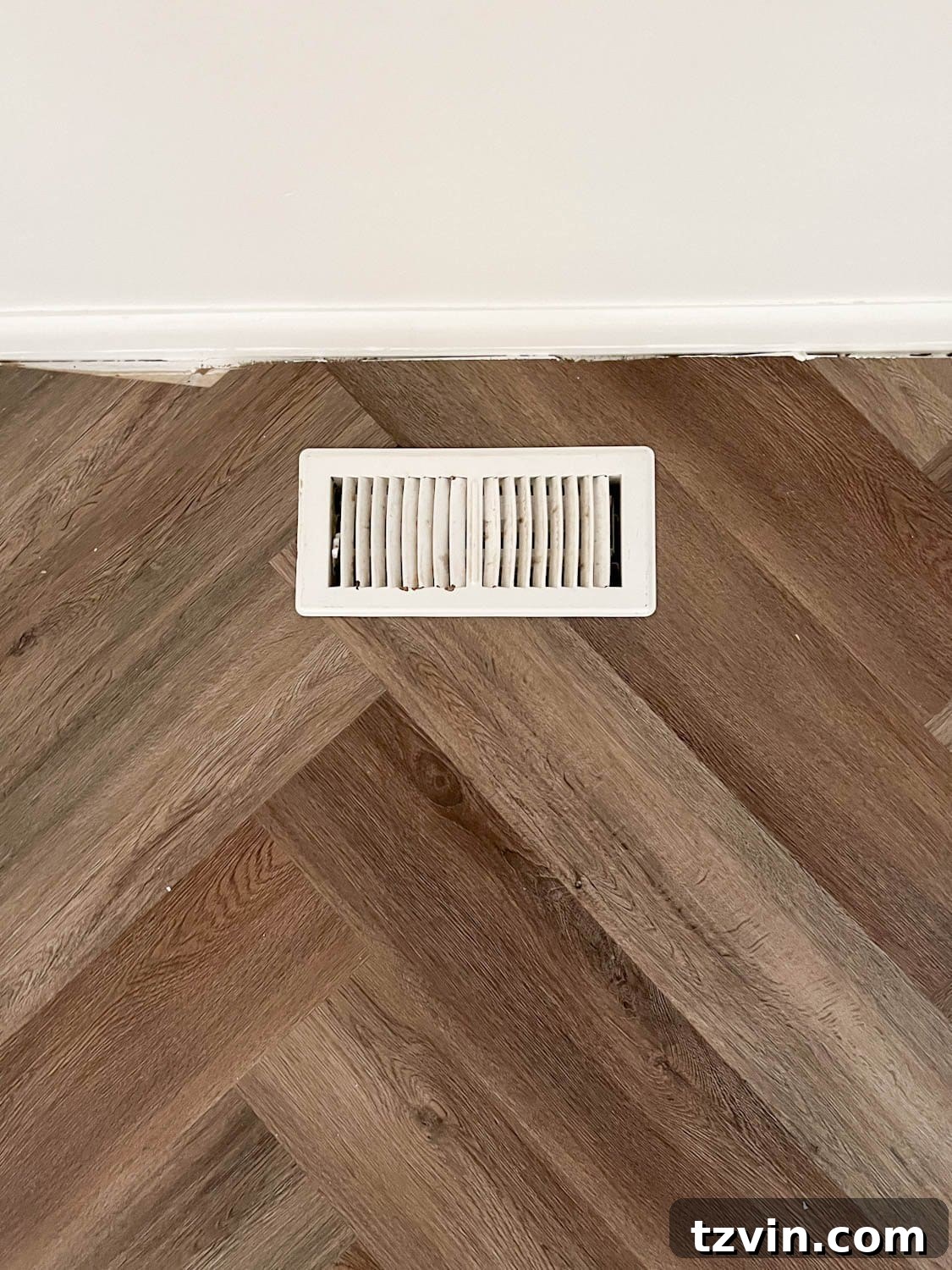 floor vent against a wall on herringbone flooring