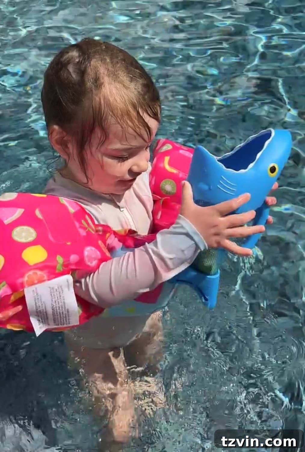 toddler girl playing with a shark pool toy game in the water