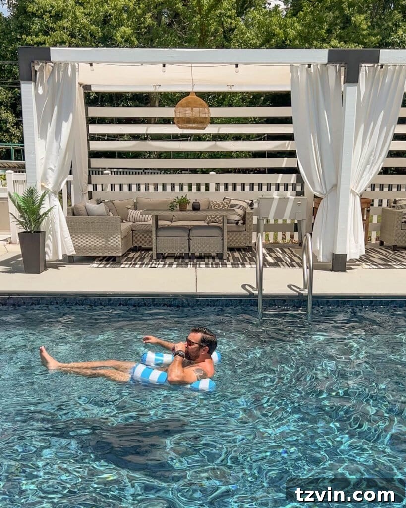 man floating on a hammock pool float in a swimming pool in front of a cabana