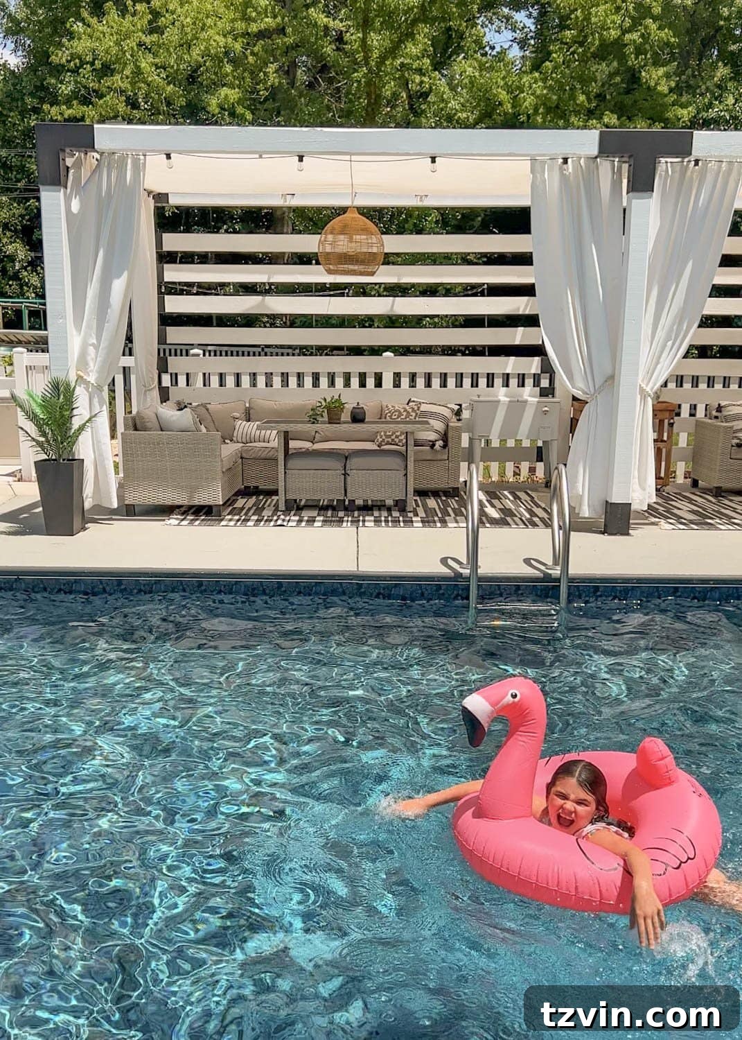 little girl playing on a flamingo pool float tube in the water in front of a cabana
