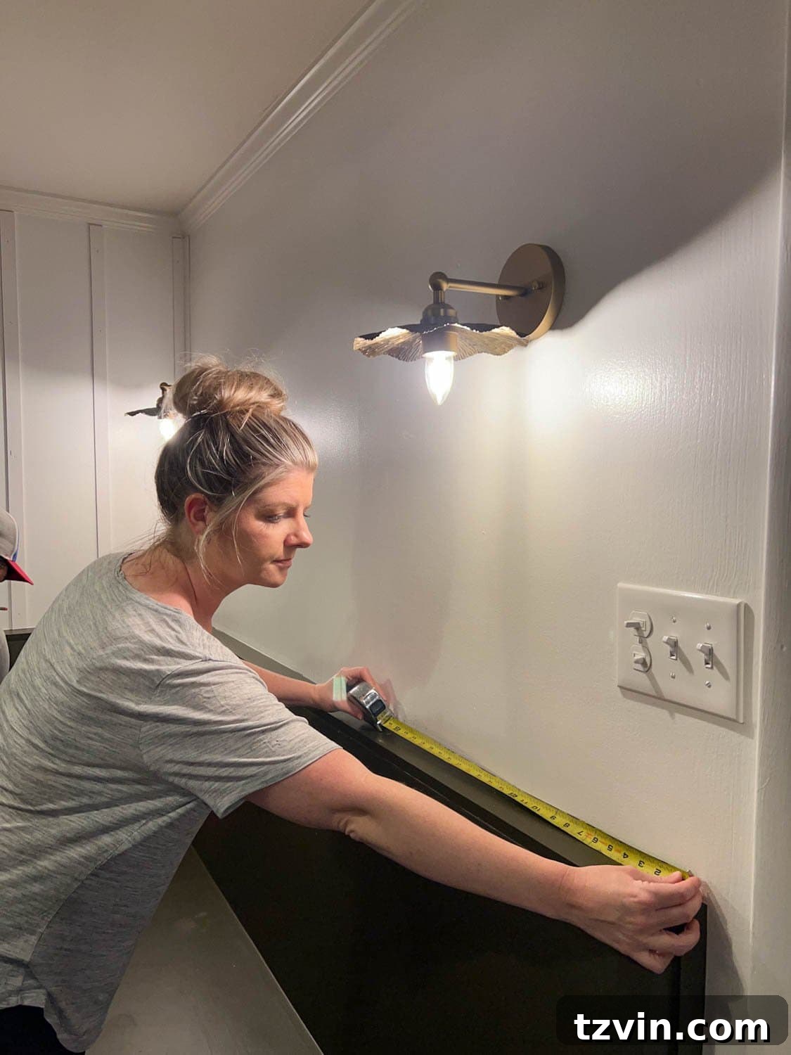 Create a Budget Batten Wall with Lattice Strips 5 A person meticulously measuring a wall with a tape measure to plan the placement of lattice strips for a DIY batten wall