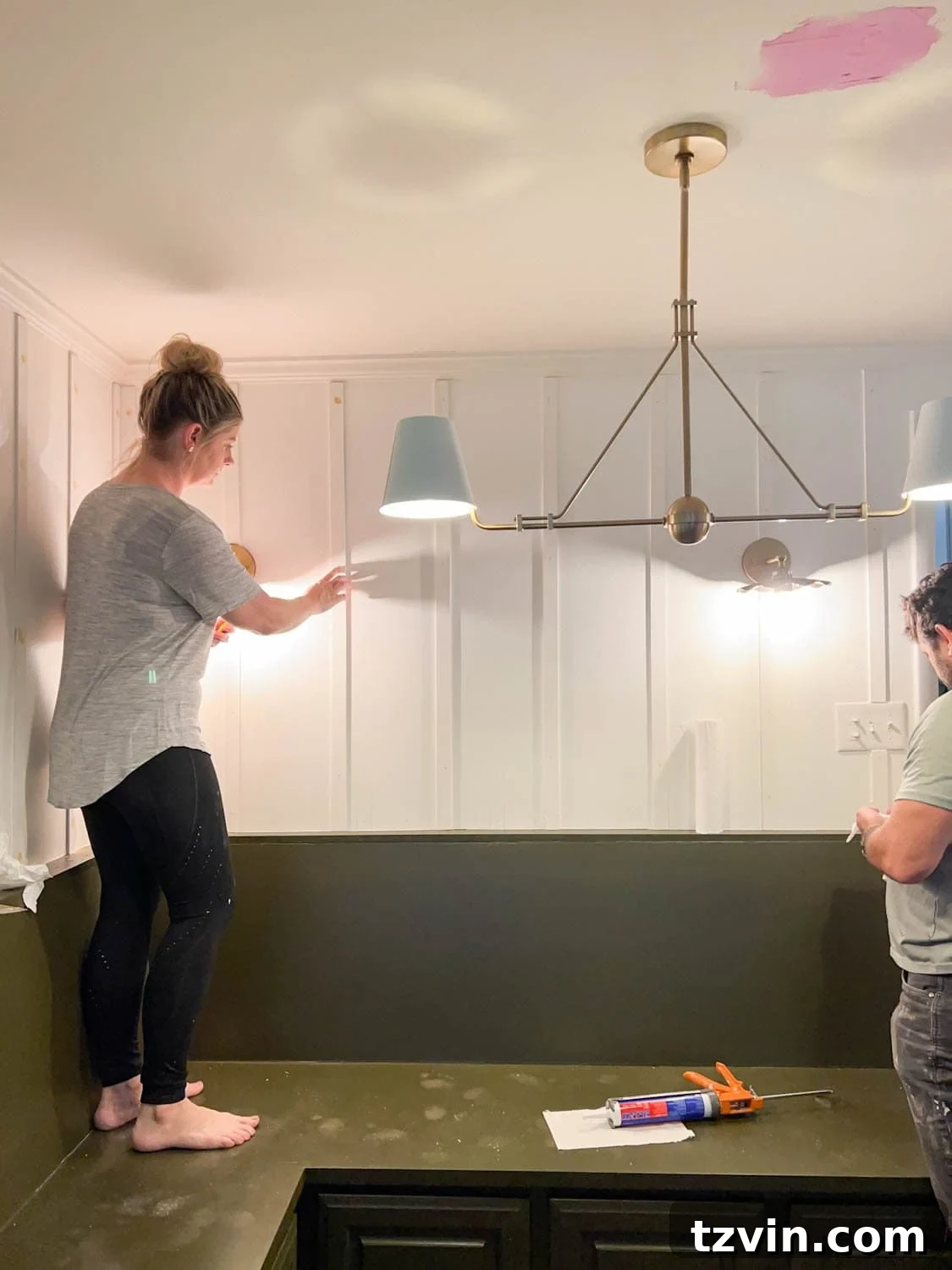 Create a Budget Batten Wall with Lattice Strips 9 A hand applying caulk to the edges of lattice strips and filling nail holes with wood filler on a batten wall