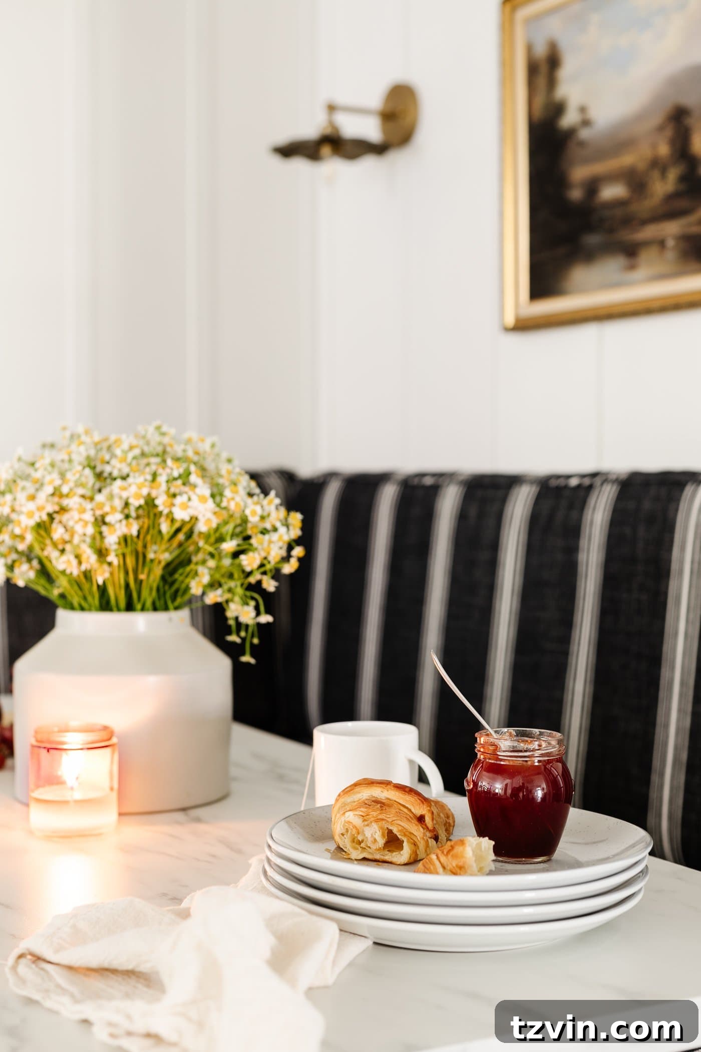 Kitchen and Nook Amazing Makeover 16 Close-up of breakfast table decor, showcasing a vase of daisies, a wood cutting board with freshly baked croissants, a bowl of ripe grapes, and a glowing candle, creating a warm and inviting scene.