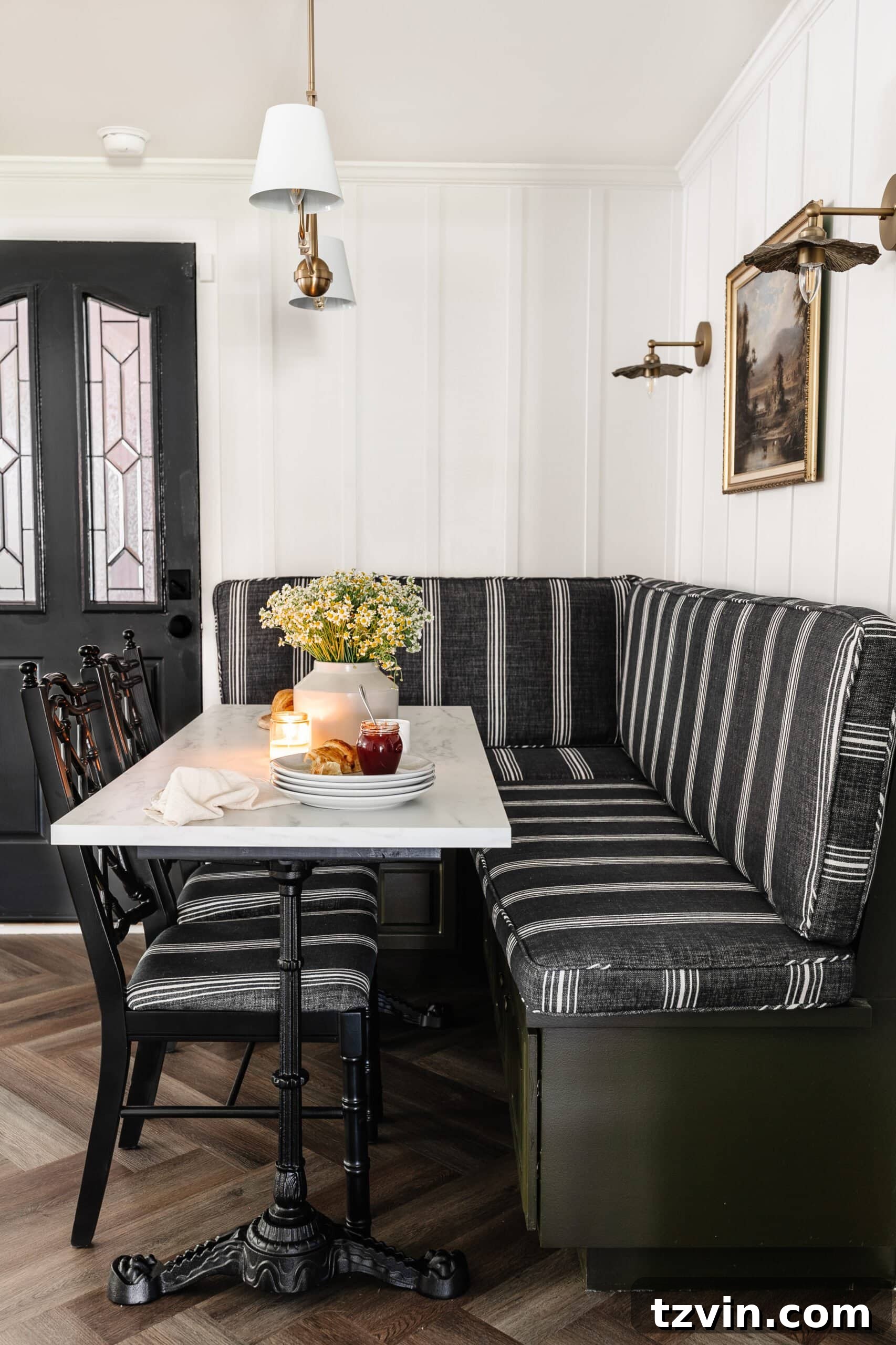 Kitchen and Nook Amazing Makeover 17 Inviting corner breakfast nook featuring a striped banquette bench, elegant batten walls, sophisticated black doors, and a charming marble bistro table, creating a perfect blend of style and comfort.