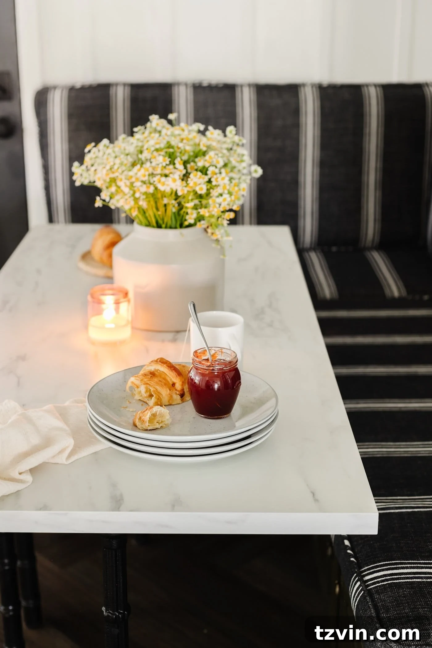 Chic Parisian Morning Retreat 12 Close-up of a marble dining table top adorned with stacked plates and a charming vase of daisy flowers