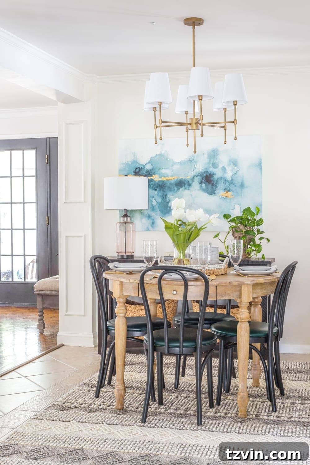 Chic Parisian Morning Retreat 20 Small dining room setup with sleek black bentwood chairs, a rustic wood dining table, vibrant blue watercolor art, and a sophisticated brass shaded chandelier