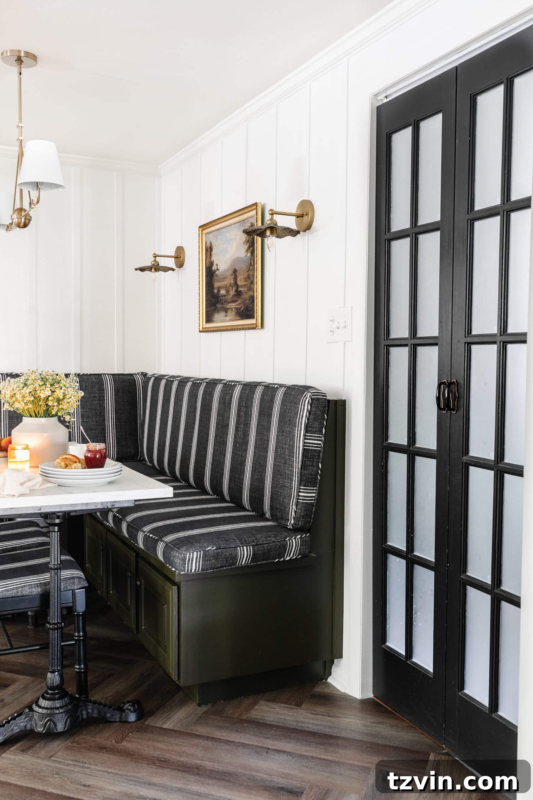 Chic Parisian Morning Retreat 5 Cozy breakfast nook featuring a comfortable booth, elegant batten wall, vintage oil painting art, practical bifold French door, and a charming Parisian bistro table