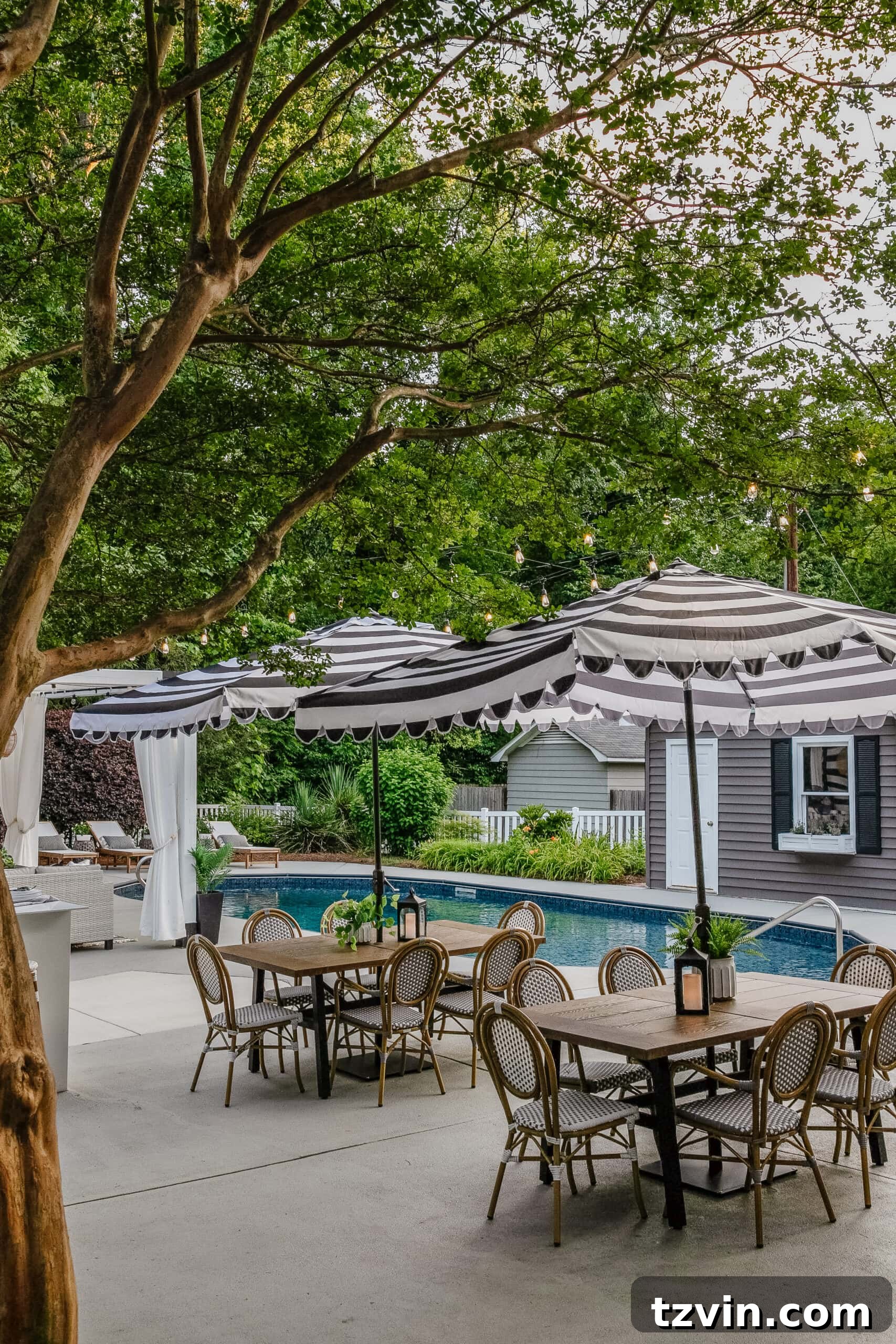 A vibrant backyard swimming pool area featuring multiple outdoor dining sets, a stylish striped umbrella, a refreshed pool shed with painted vinyl siding, a beautifully painted concrete deck, comfortable poolside patio furniture, and a charming cabana, creating a luxurious and inviting outdoor retreat.