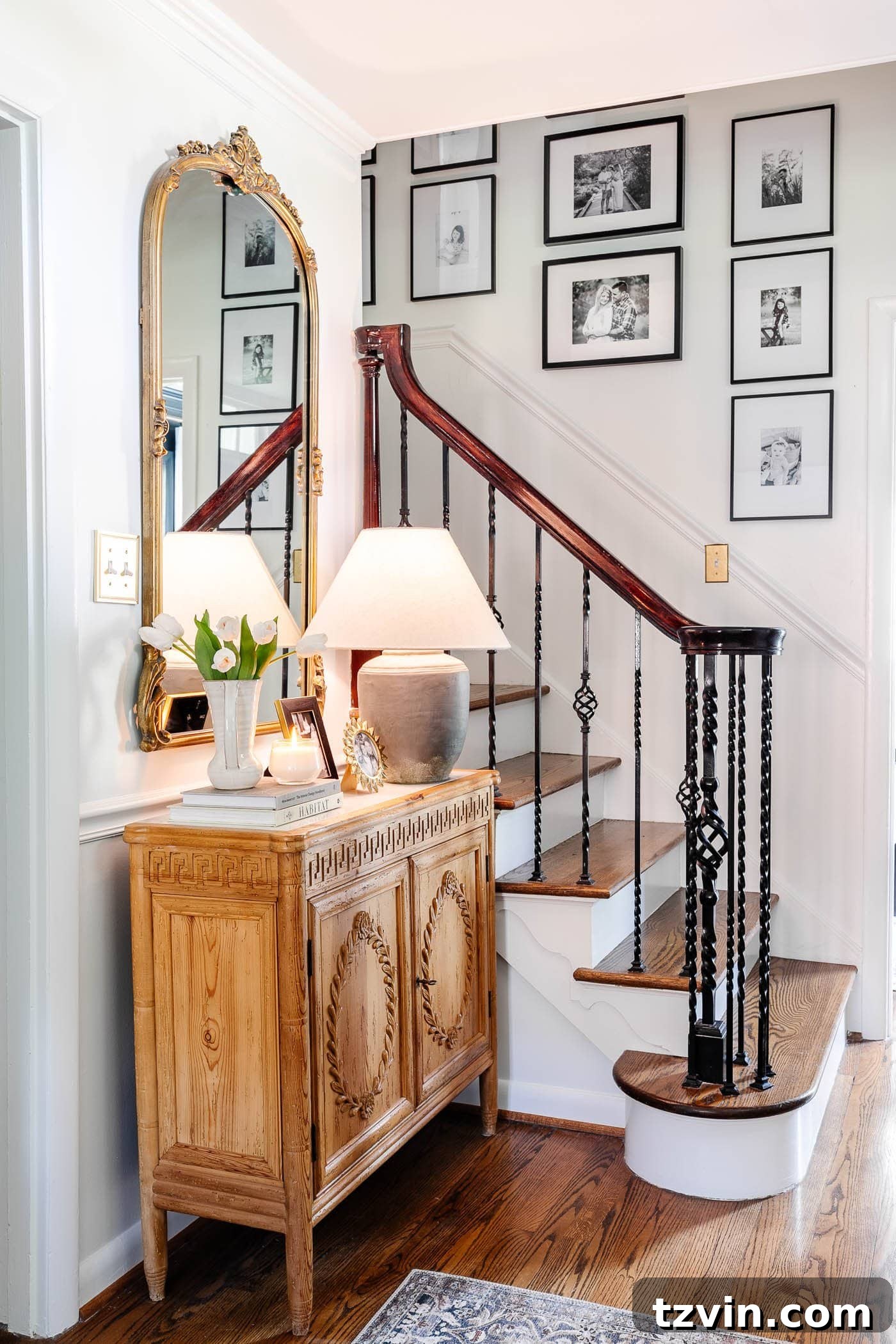 Transformed foyer and front entryway with white walls and a striking carved wood cabinet adorned with an ornate gold mirror, creating a refined and elegant atmosphere.