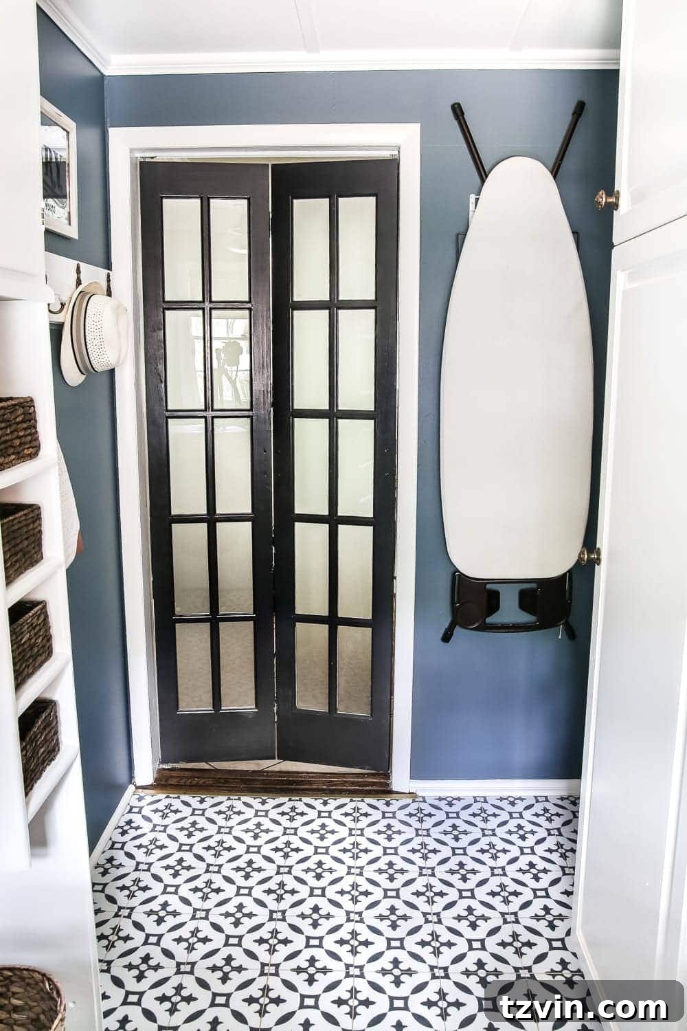 A vibrant navy blue laundry room featuring black and white Moroccan peel and stick tile floors and an elegant black bifold French door, creating a stylish and functional space.