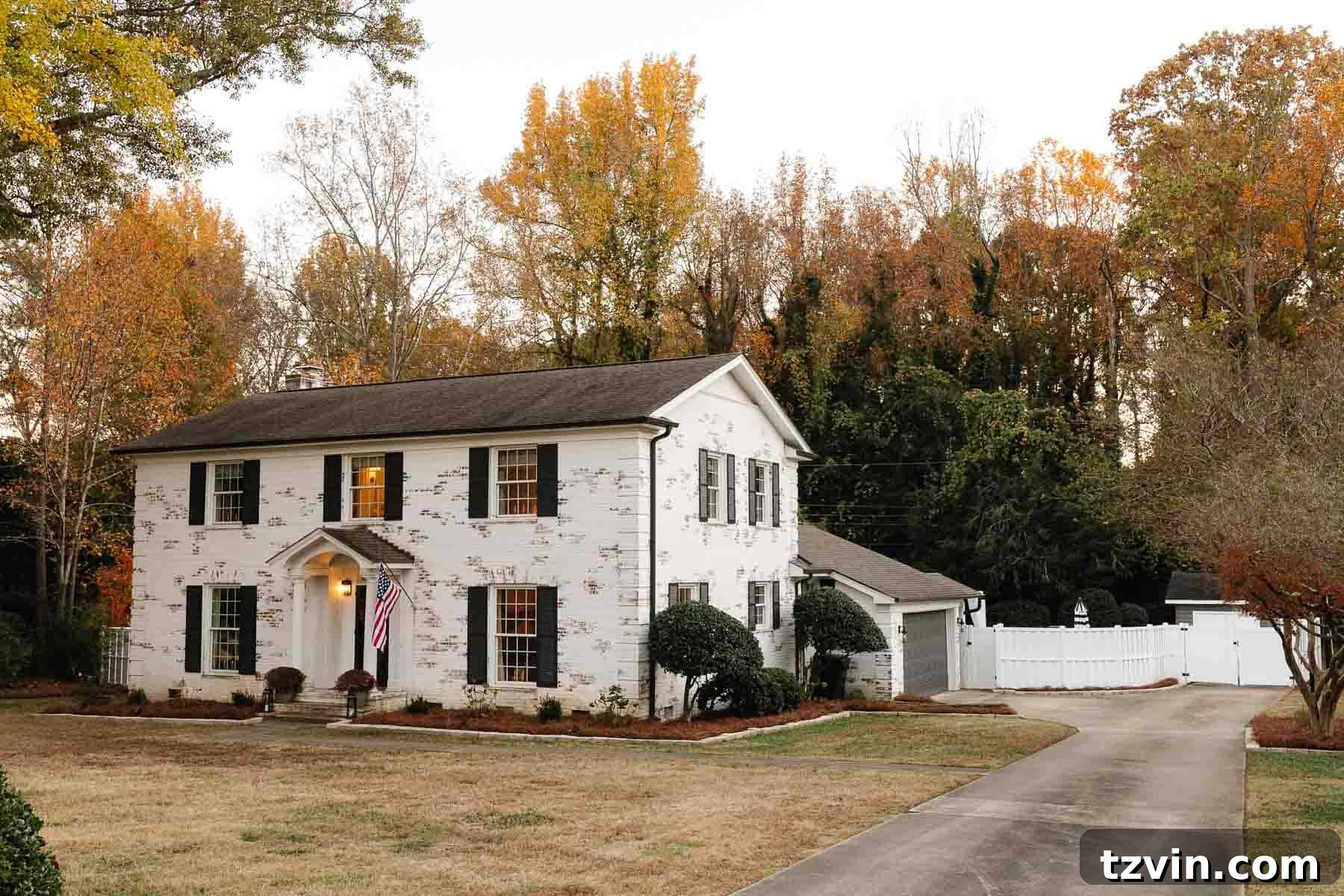 Stunning white limewashed brick colonial house featuring contrasting black shutters and doors, complemented by a pristine white vinyl fence, creating a modern farmhouse aesthetic.