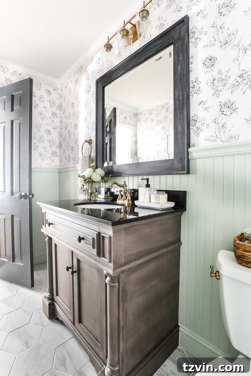 A charming mint green beadboard half bath featuring elegant black and white floral wallpaper, a sophisticated faux marble hexagon tile floor, and a rich wood vanity, creating a stylish and inviting space.