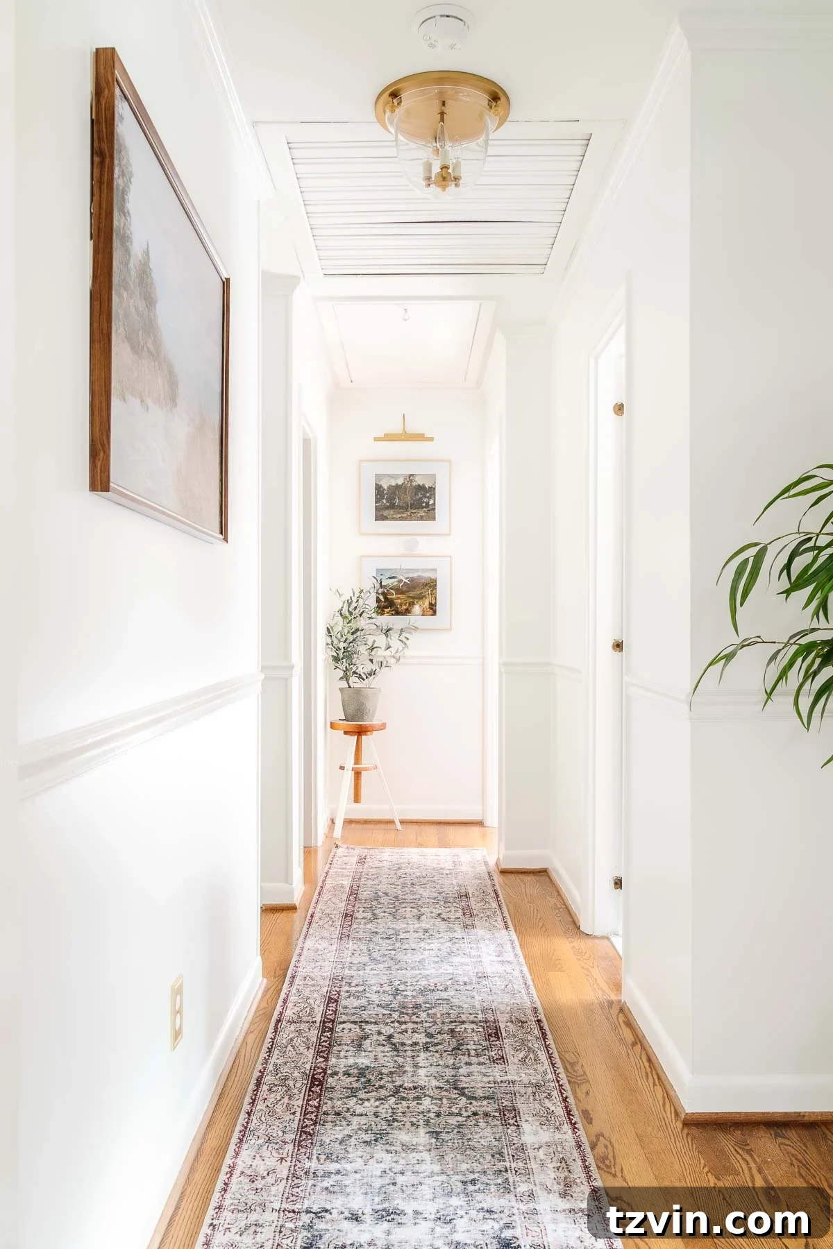 A bright white hallway featuring contrasting black doors, a vintage runner rug, an elegant brass light fixture, and charming landscape art, creating a stylish and inviting transitional space.