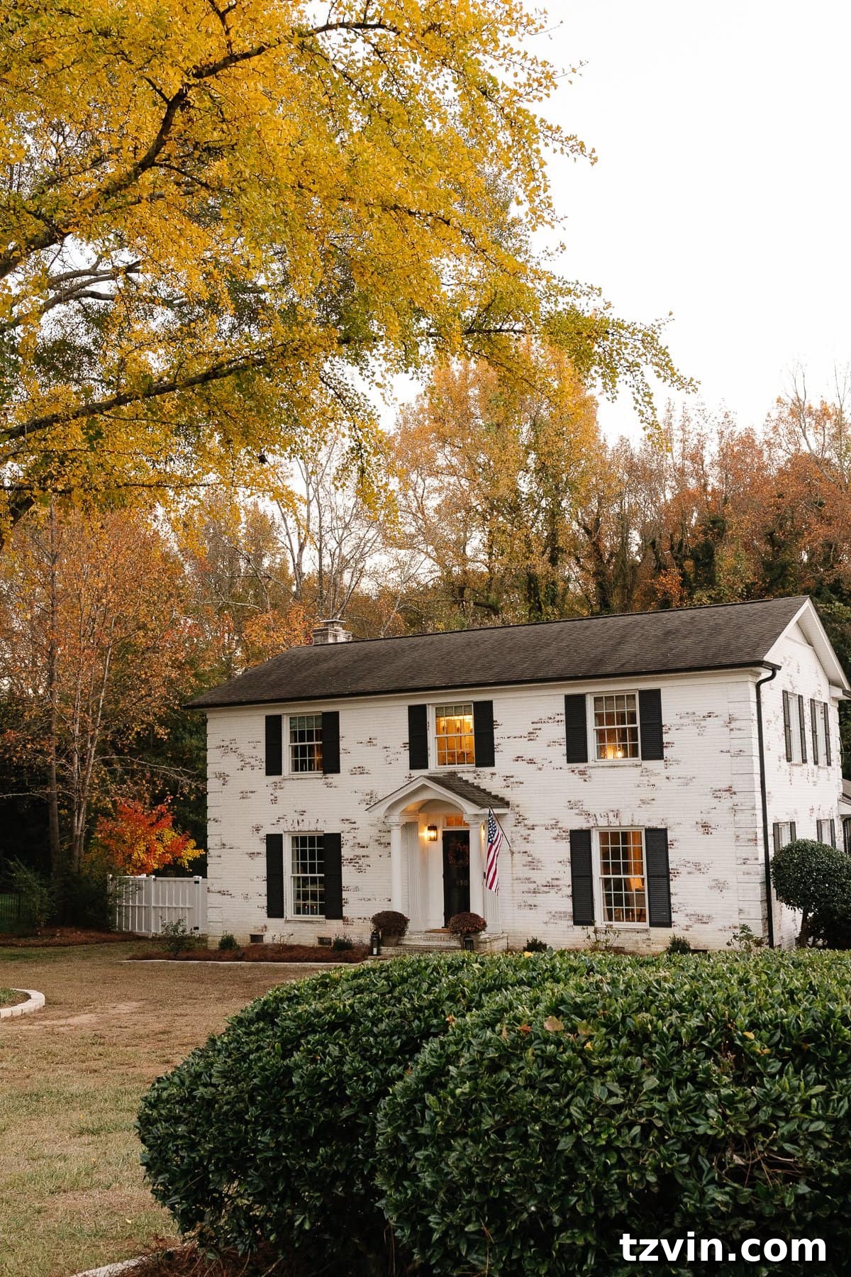 Elegant white limewashed brick colonial house featuring bold black shutters and doors, perfectly framed by a crisp white vinyl fence, showcasing a complete exterior makeover.