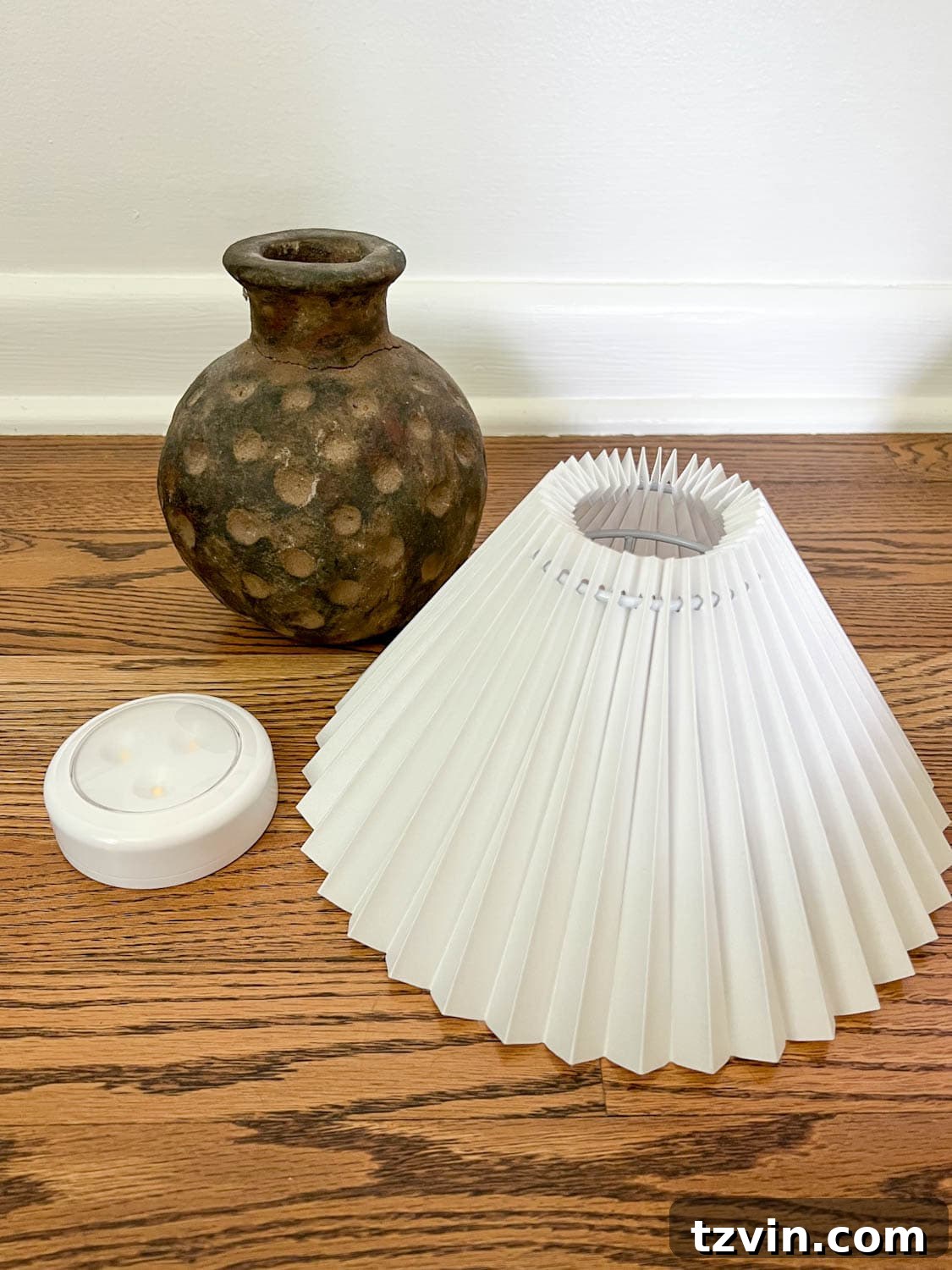 The three essential components for a cordless DIY lamp: a rustic terracotta vase, an elegant pleated lamp shade, and a compact puck light, ready for assembly.