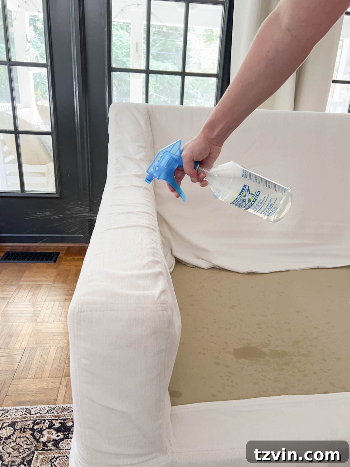 Spraying DIY couch cleaner solution onto sofa upholstery to clean off dirt and grime.