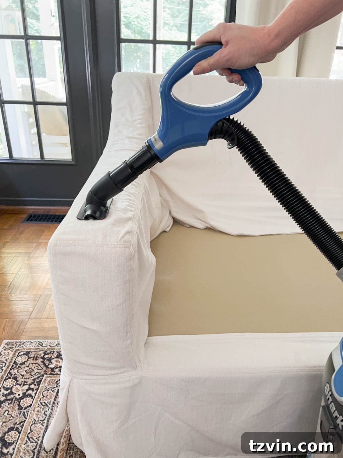 Vacuuming a sofa slipcover with a wand attachment to remove baking soda, hair, dirt, and lint after deodorization.
