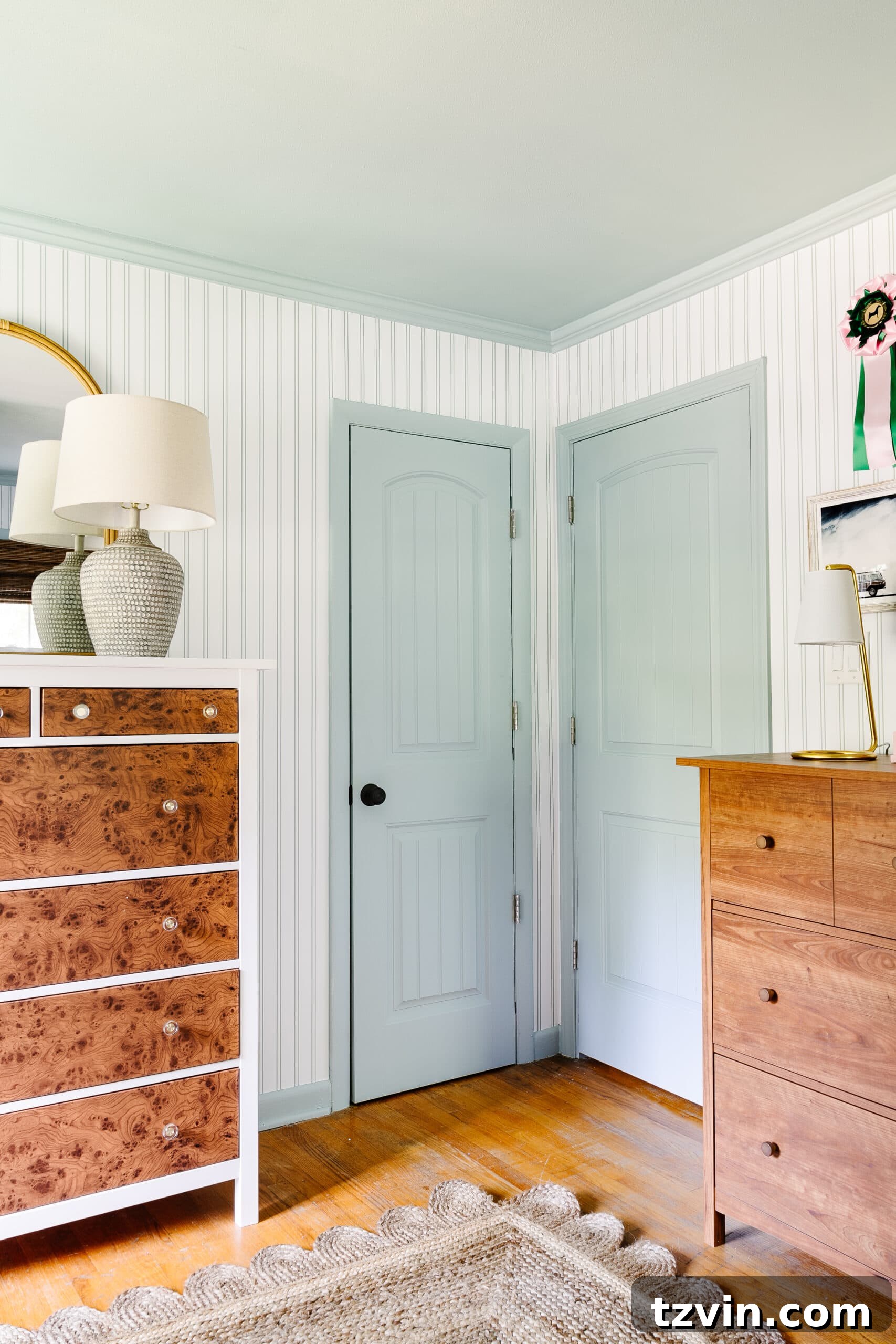 Blue doors, trim, and ceiling paired with striped wallpaper and wooden dressers in a charming shared teenage beach themed bedroom