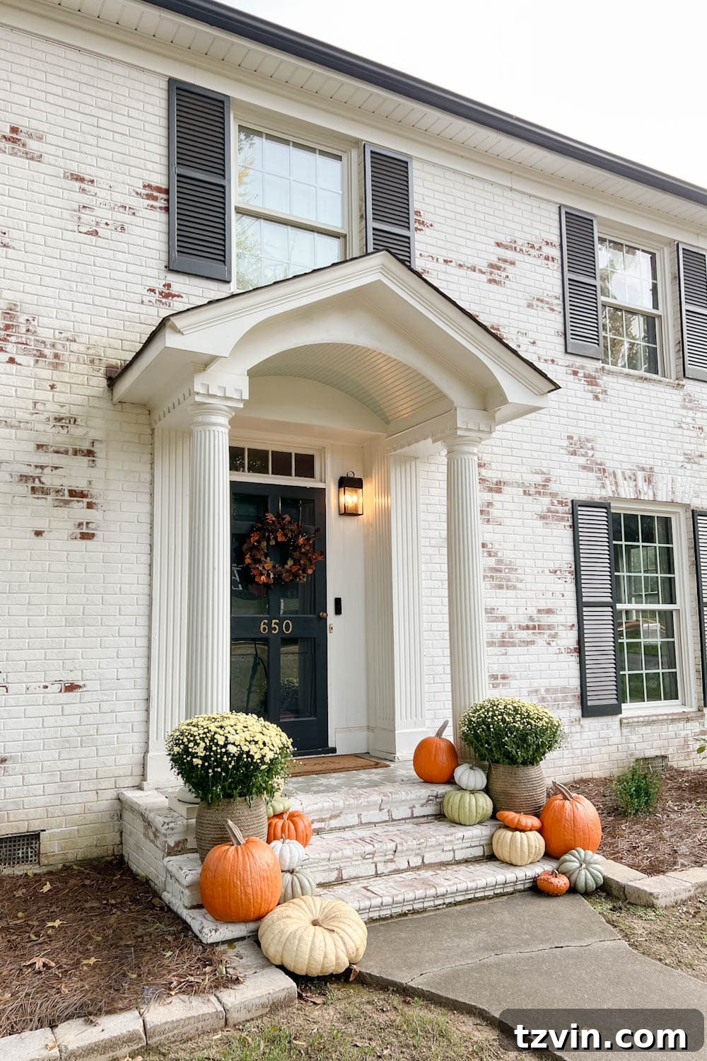 Harvesting Realism: The Top Fake Pumpkins of 2024 5 A colonial-style home with limewashed brick features a vibrant fall front porch, showcasing artificial pumpkins elegantly arranged on the steps and seasonal decor.