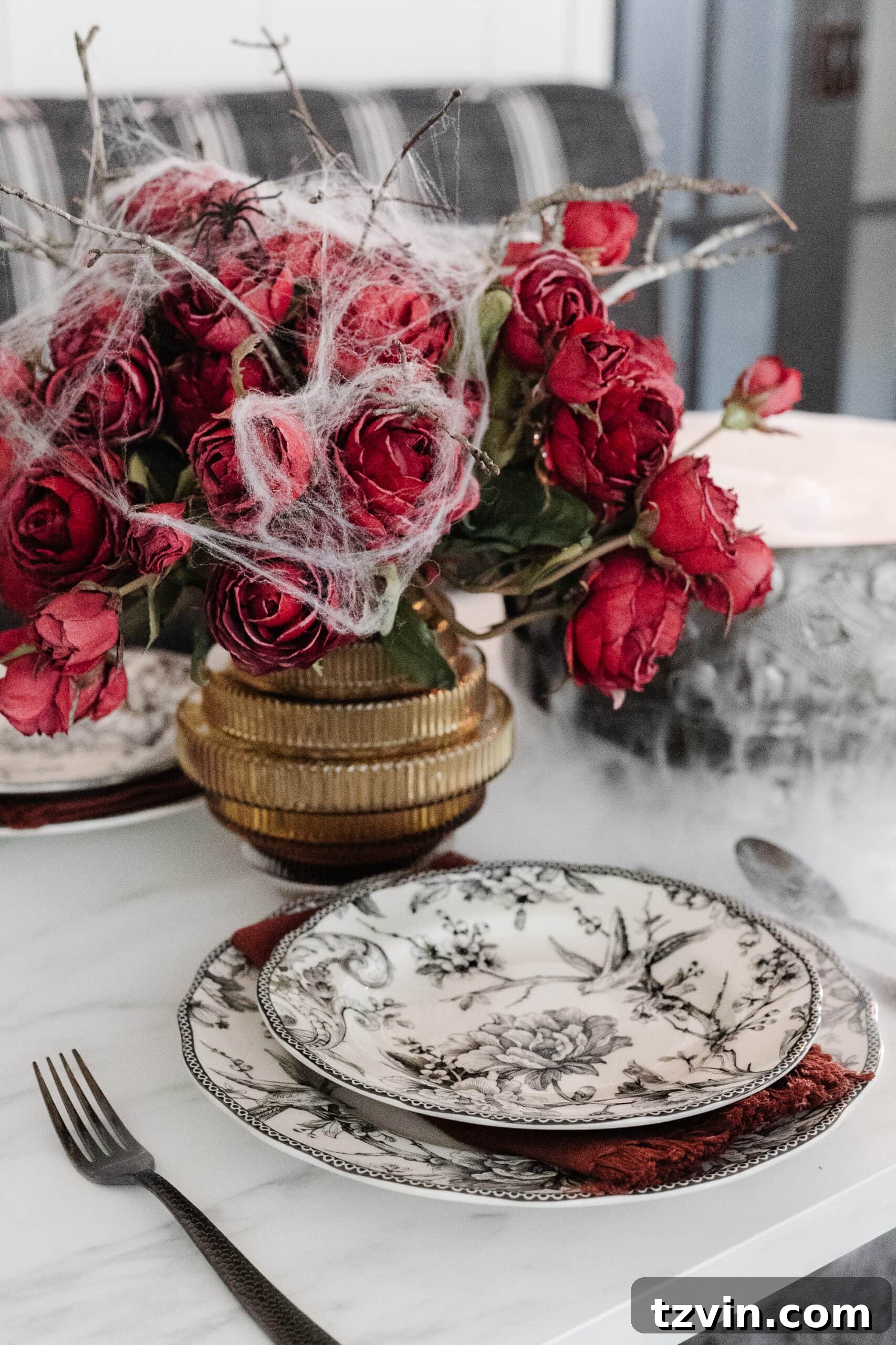 Killer Tablescapes: Spooky Settings for Your Murder Mystery Party 8 Black toile dinnerware paired with a fluted vase of red roses and spider webs, creating a gothic chic table setting