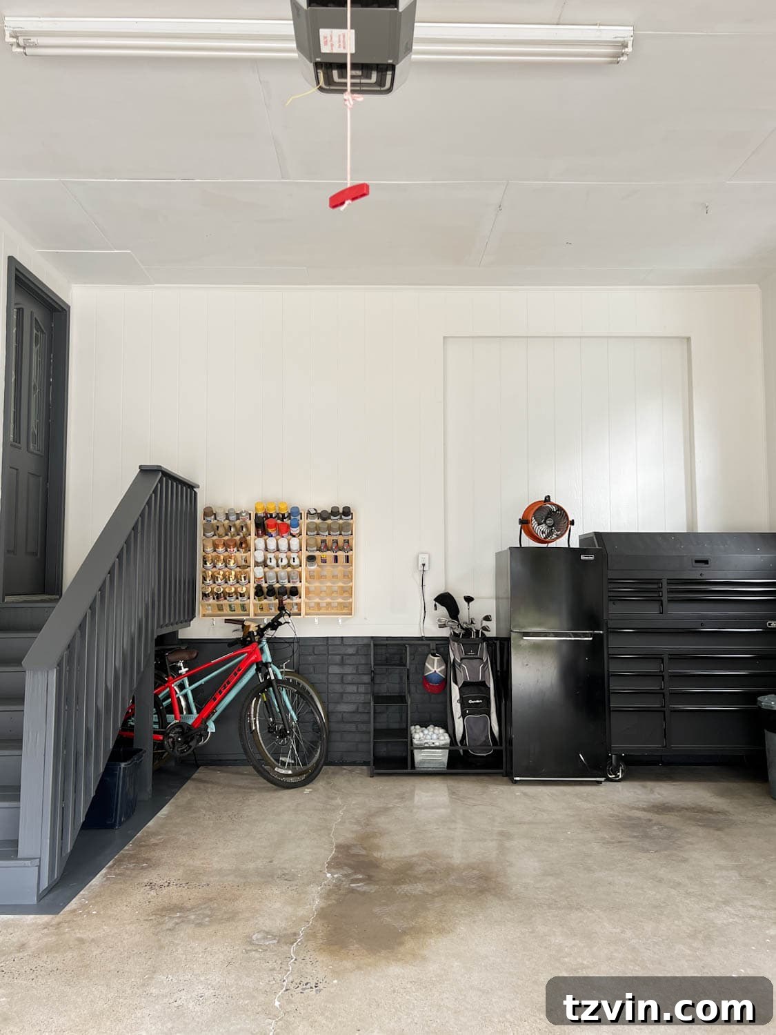 Well-organized garage after a makeover, featuring white walls, black trim, and a repurposed concrete floor, showcasing efficient storage for various items.