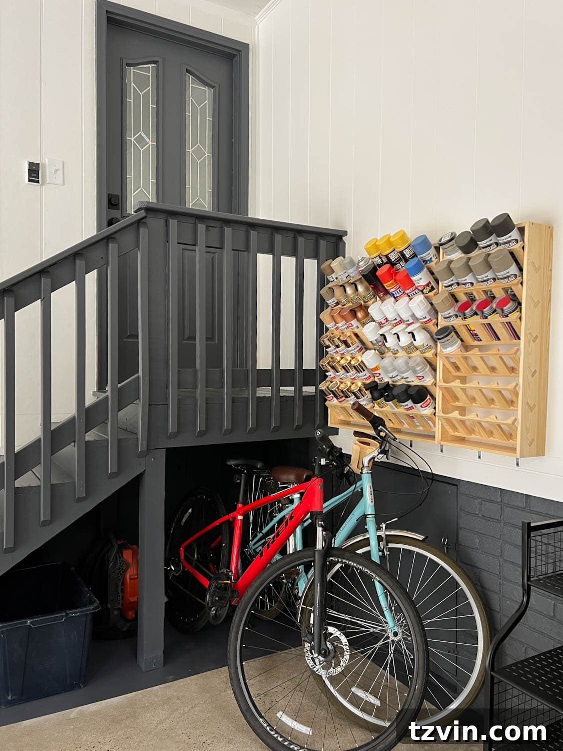 Organized paint can storage rack and bicycles neatly parked under the stairs in a renovated garage.