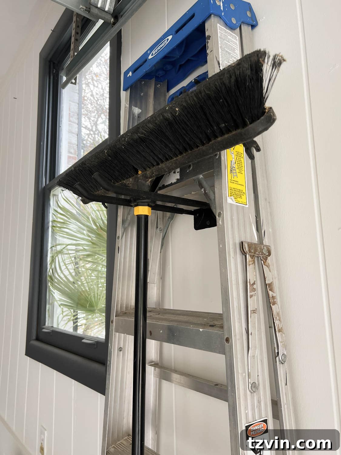 Wall-mounted hooks providing organized garage storage for various tools, including a ladder and brooms.