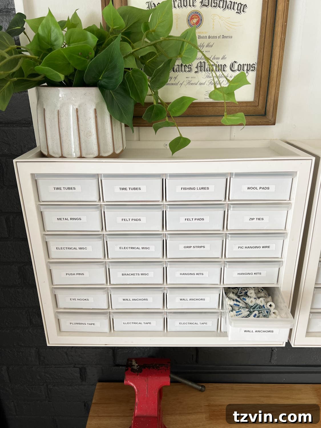 A hardware organizer mounted on a garage workshop wall, showing labeled drawers for small components.