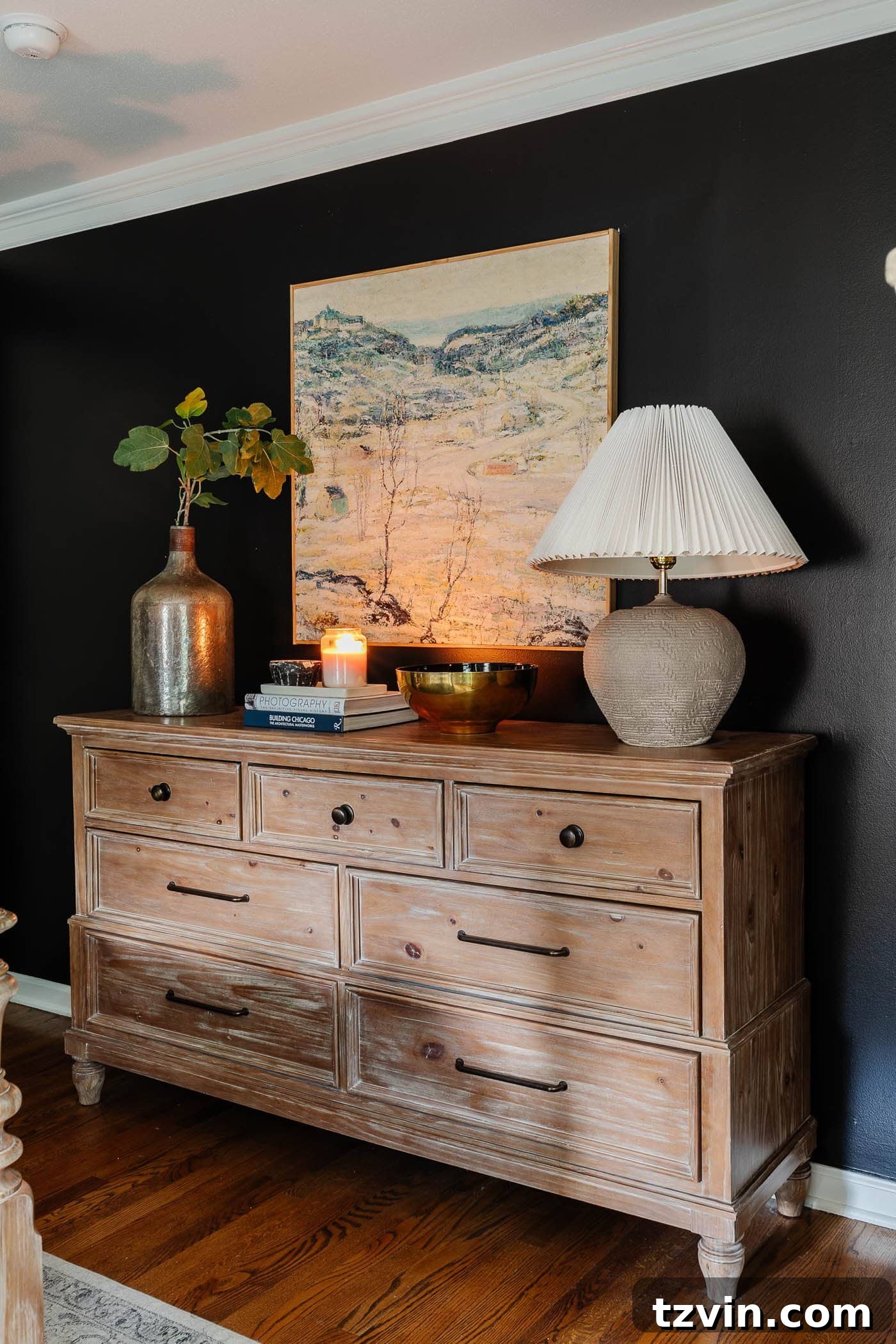 winter bedroom decor on a dresser with lamp, art, candle, and vase of greenery