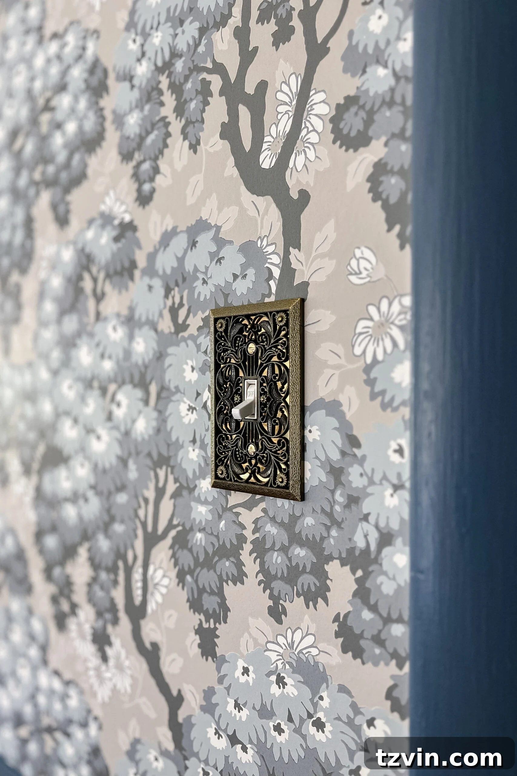 Ornate vintage light switch cover complementing floral Swedish wallpaper