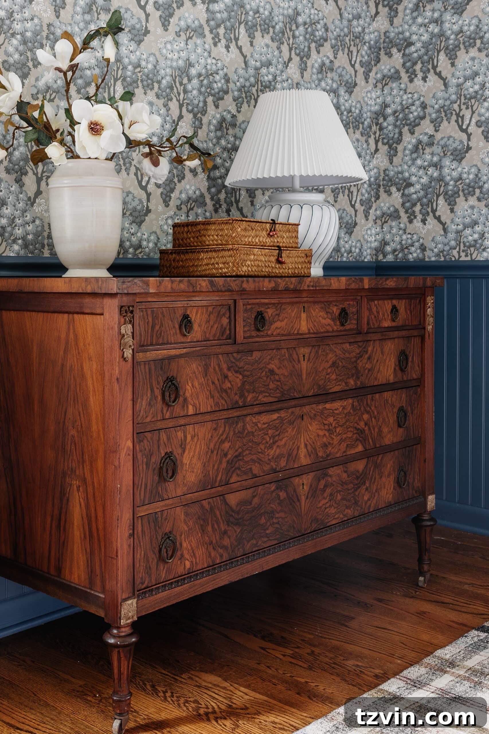 Discover Affordable Burl Wood Furniture Including Refinished Dressers 5 burl wood dresser styled with vase of flowers woven basket boxes and lamp in a bedroom with blue vintage wallpaper