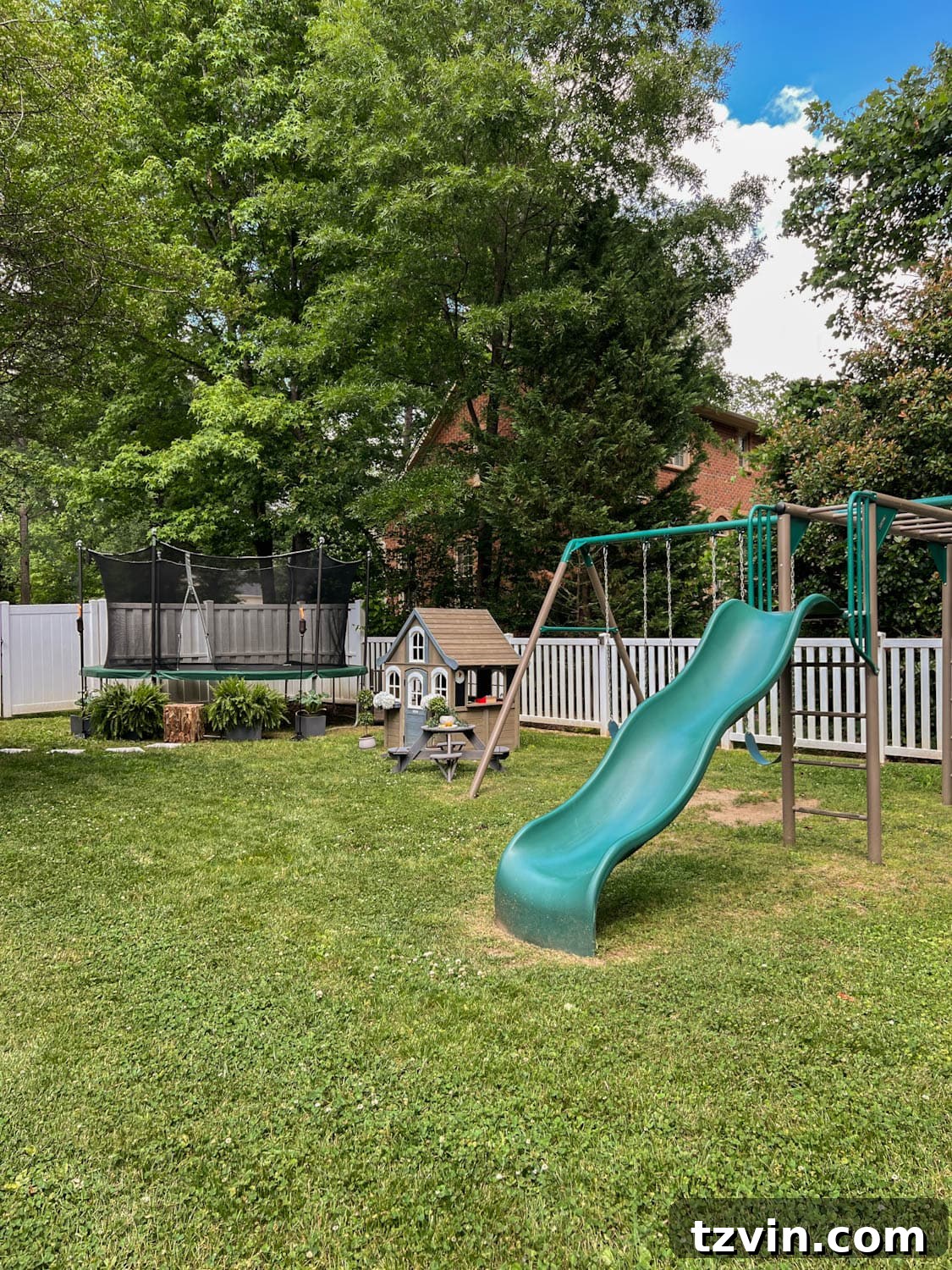 Spacious side yard play area for kids, featuring a vibrant trampoline, an inviting outdoor playhouse, and a sturdy swing set, surrounded by greenery.