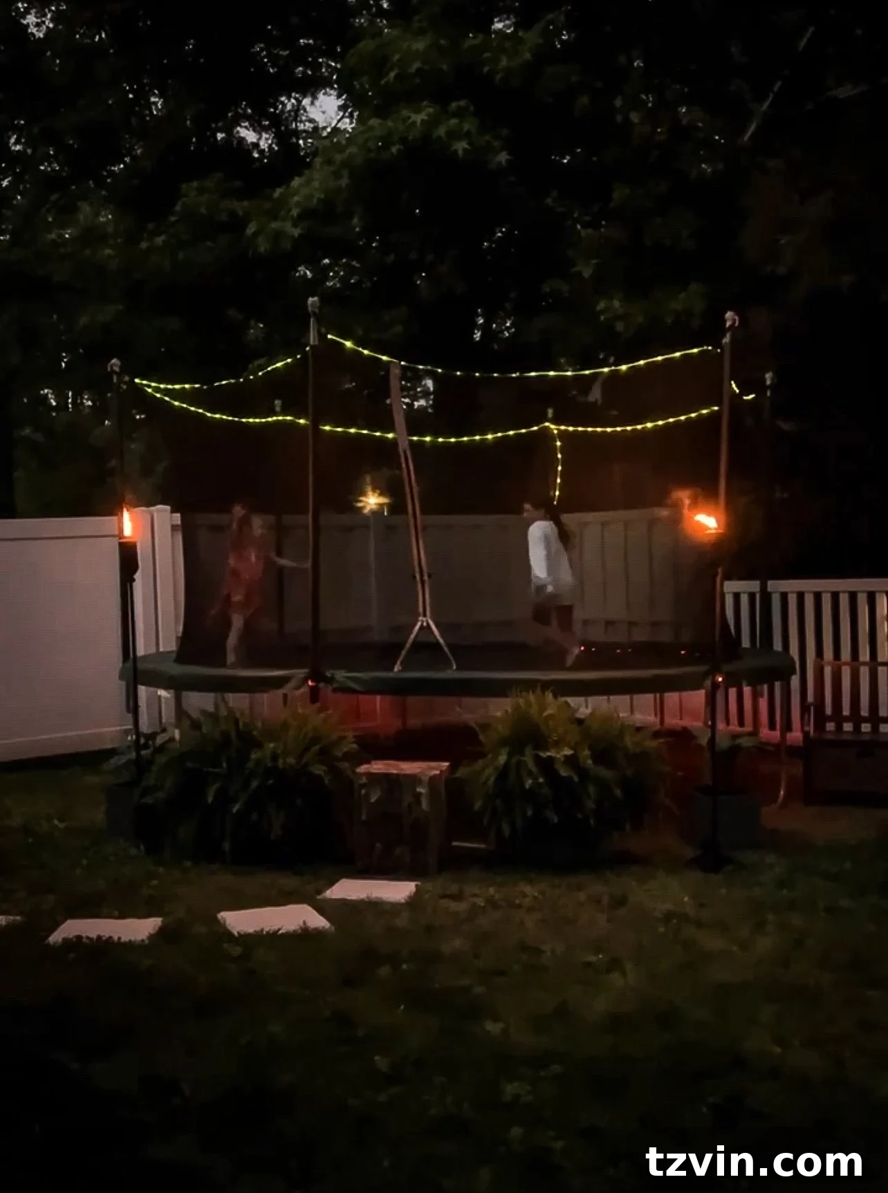A vibrant backyard trampoline illuminated with colorful lights at night, creating a magical play experience in the side yard.