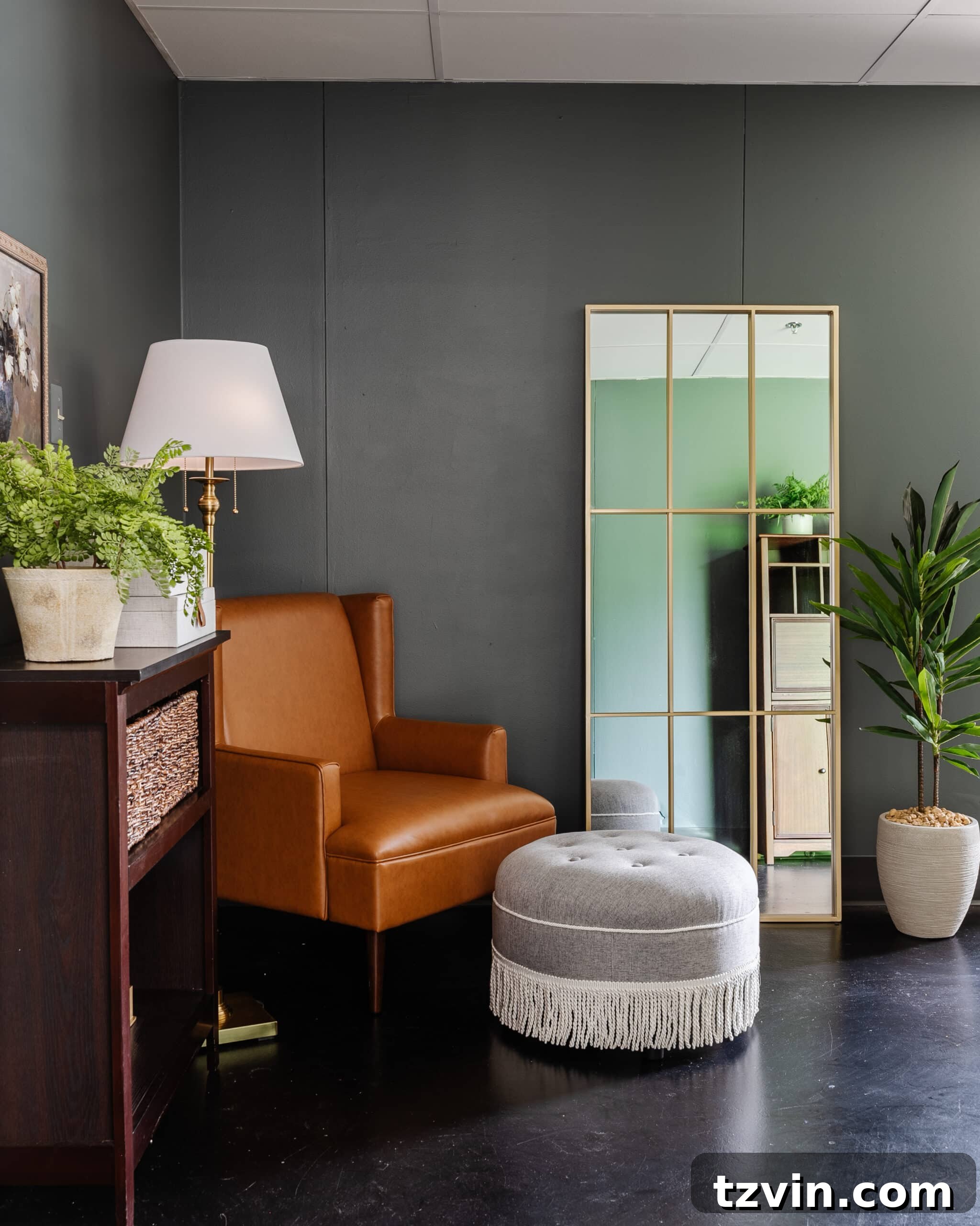 Warm Up Your Workday Cozy Conference Room Ideas for an Office Refresh 21 A cozy reading corner in an office featuring a leather armchair and fringe ottoman, strategically placed next to a full-length mirror that enhances light and space.