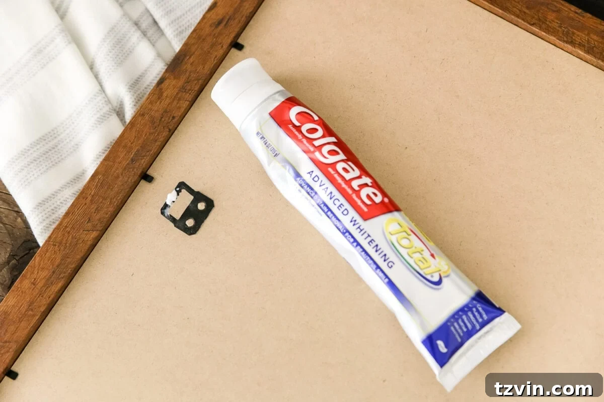 Hang Frames Perfectly Avoid These Common Errors 6 The 'toothpaste trick' being used to precisely mark a spot on the wall for hanging a picture, minimizing errors.