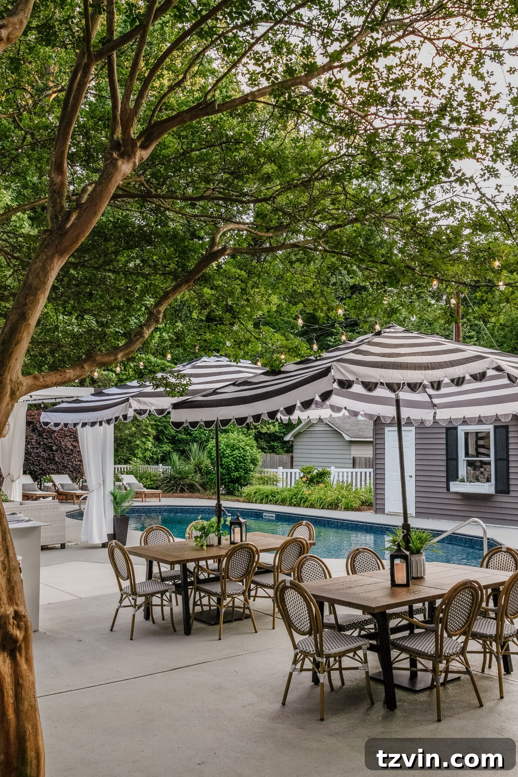 patio dining tables and chairs with striped umbrellas for shade around a backyard pool